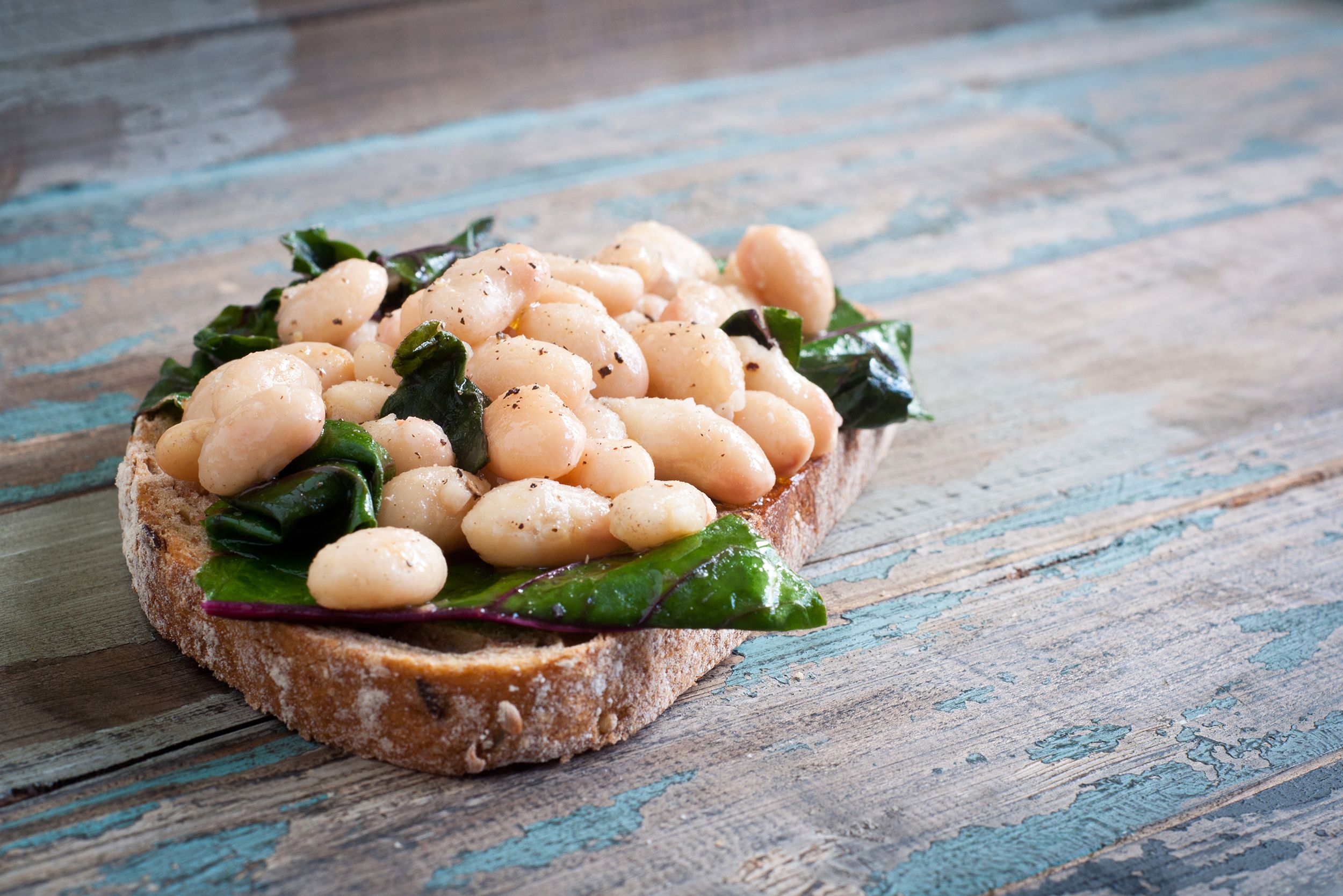 Half of white bean arugula sandwich on one slice of bread, selective focus, on the left-center, on a partially blue painted rustic wooden table