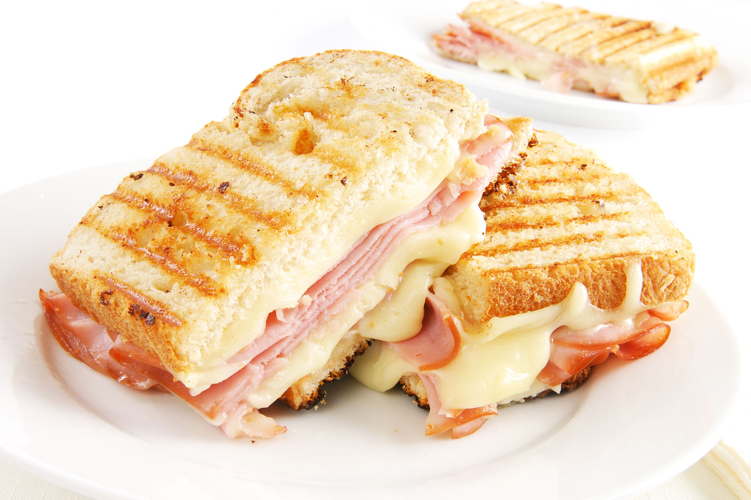 Ham and cheese sandwich, cut in half, on a white porcelain plate, on a white table with another white porcelain plate with a half of ham and cheese sandwich