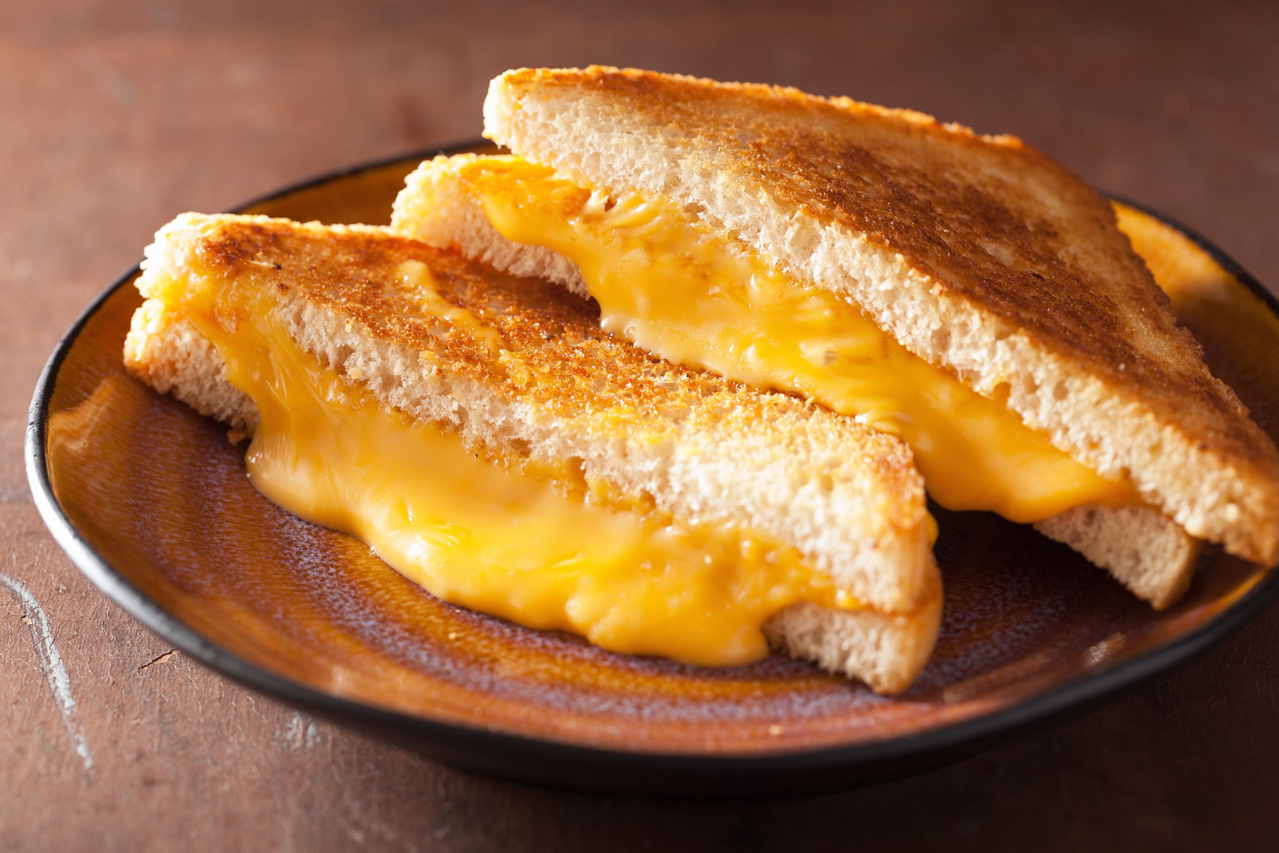 Two halves of grilled cheese sandwich on a purple and orange ceramic plate, selective focus, on a wooden table