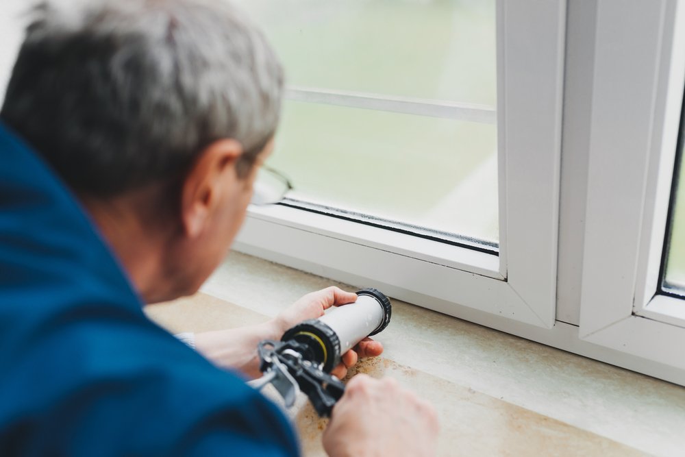man using a silicone tube for repairing the window indoor