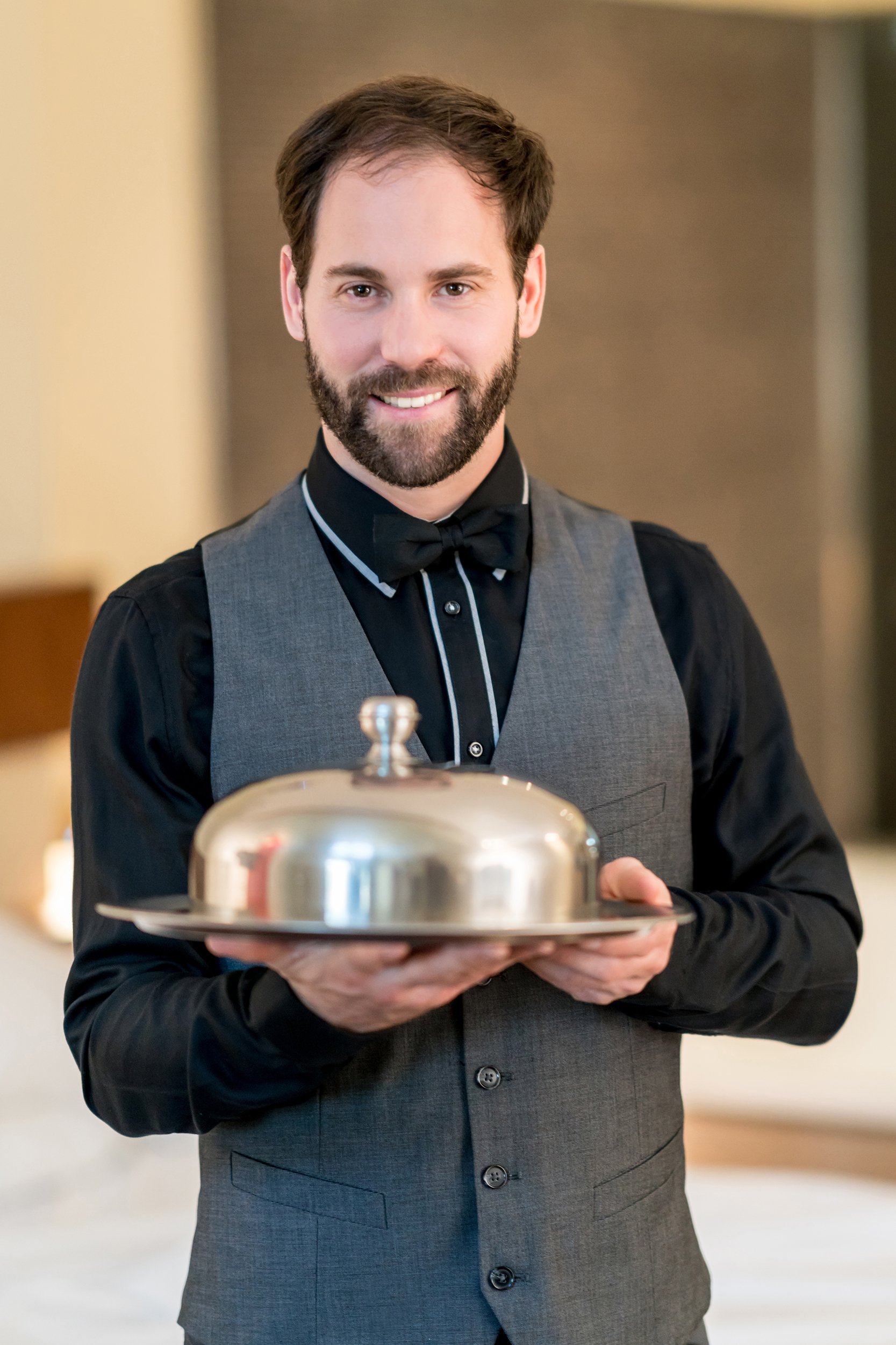 waiter at a restaurant holding a tray and looking at camera smiling
