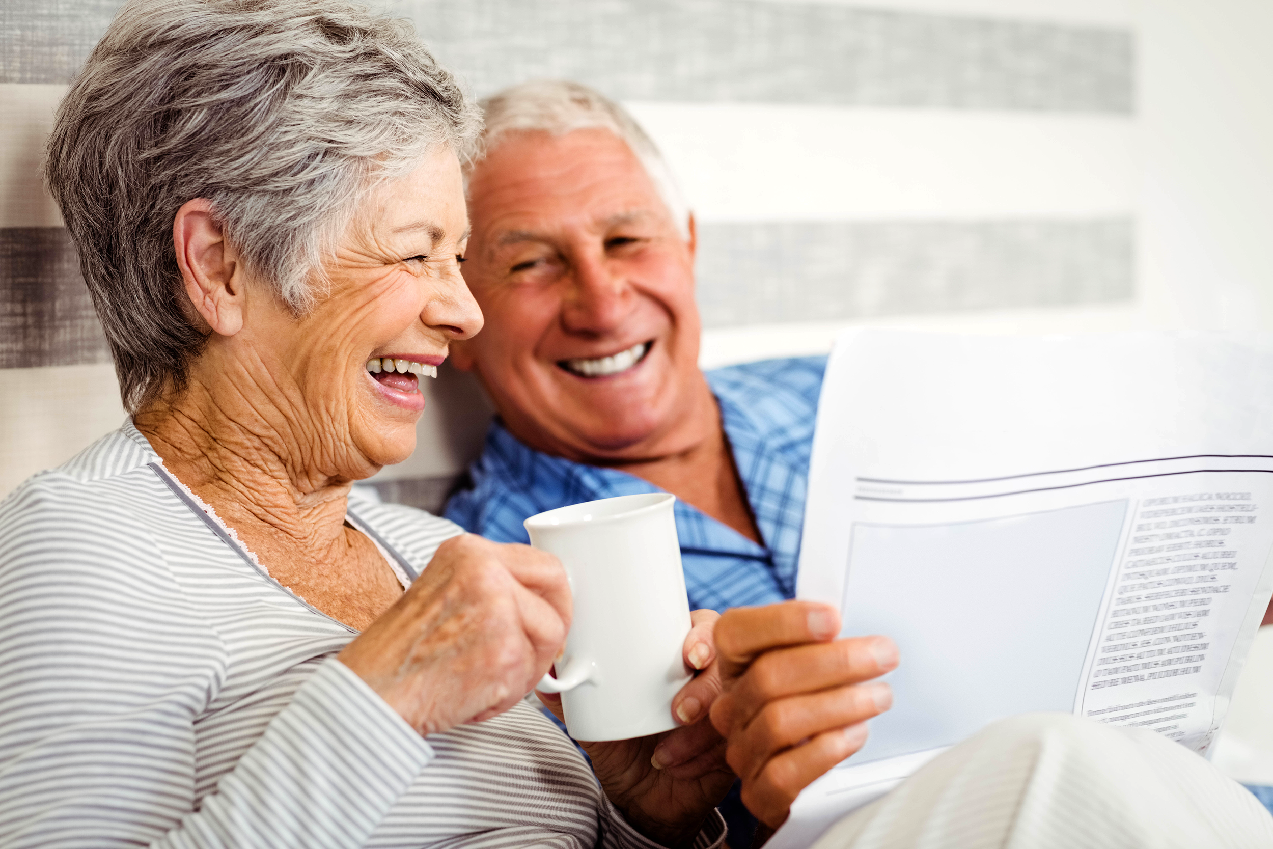 Senior couple enjoying coffee and reading the newspaper in bed