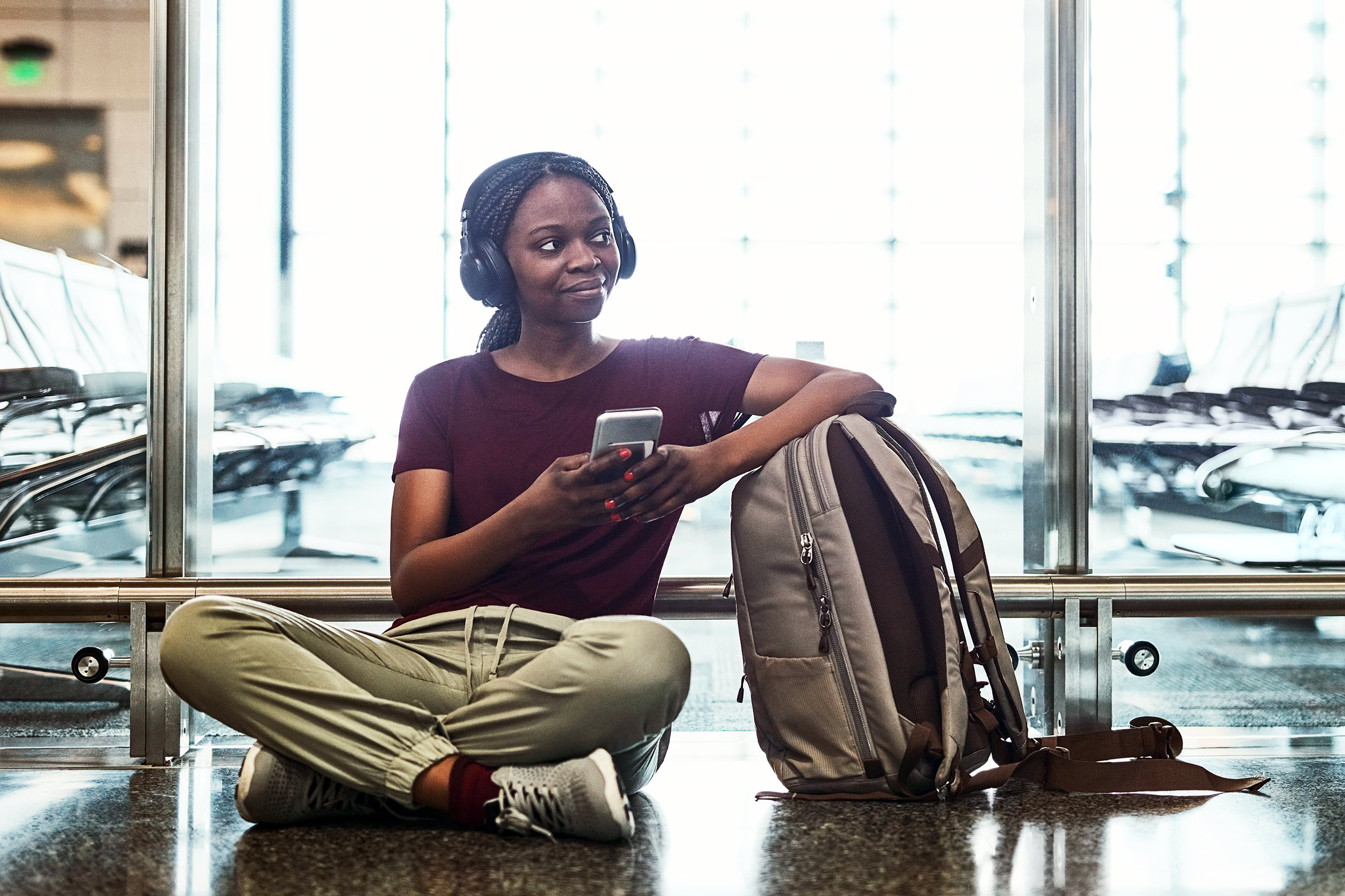 Woman sitting in an airport with her backpack listening to music