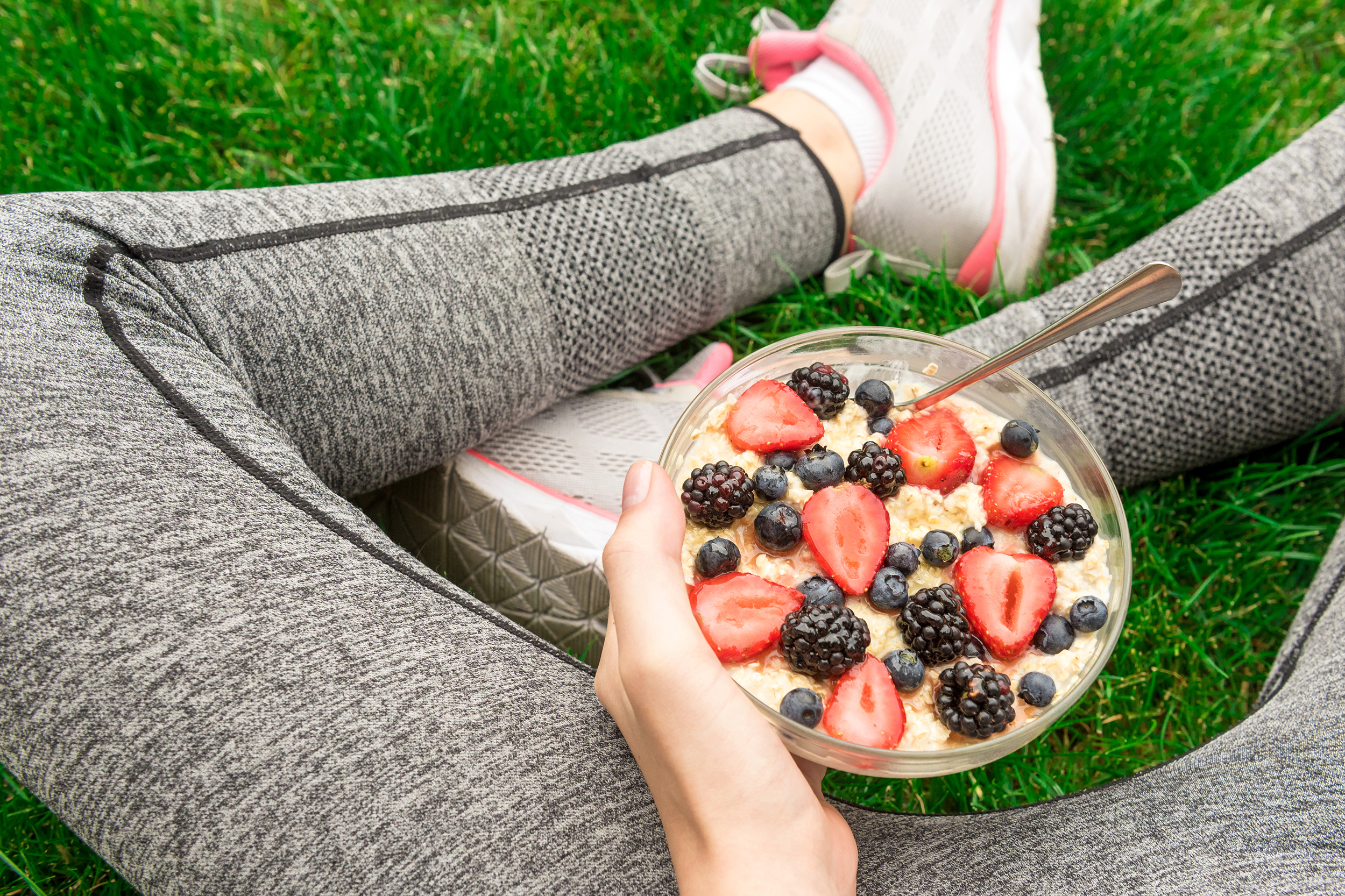 Woman sitting on the grass eating a bowl of oatmeal with fruit