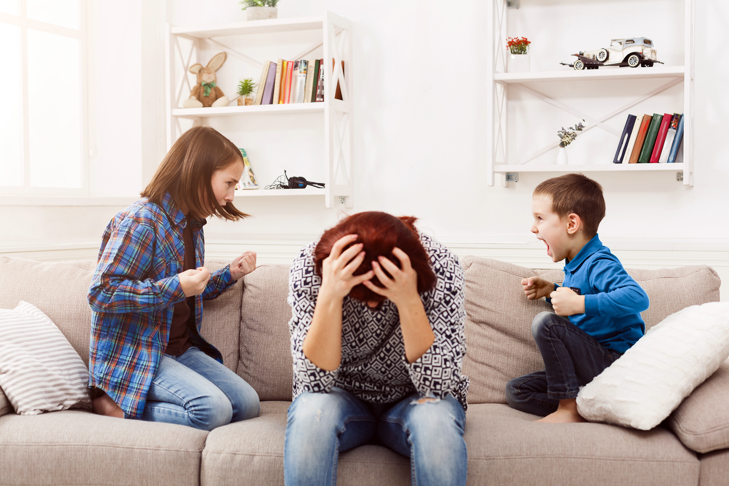 Stressed mom on the couch with her two children screaming at her