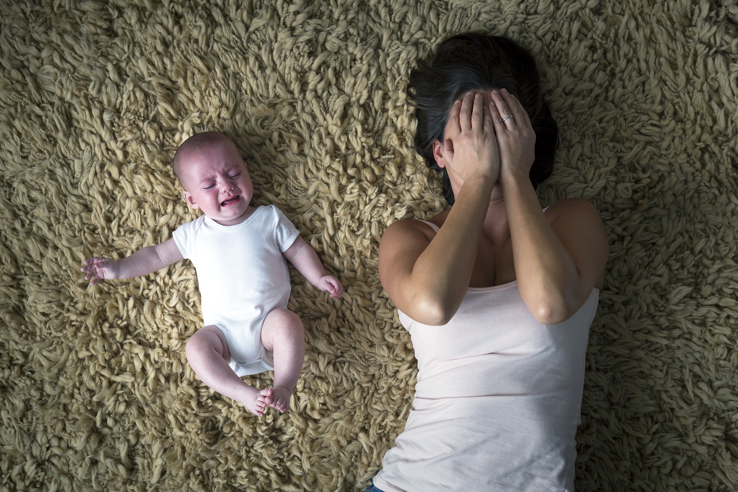 Depressed mom on the floor covering her face next to her crying baby