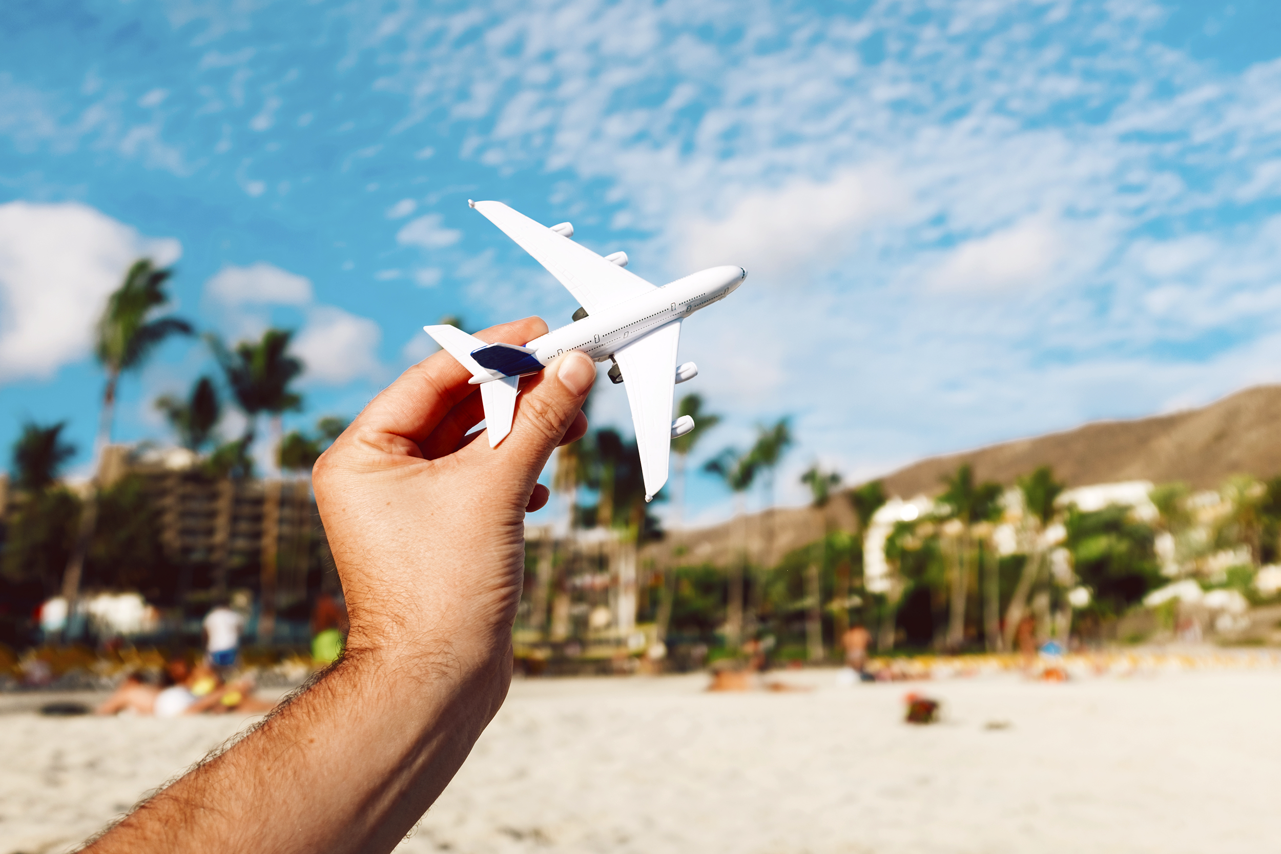 Someone on a beach holding up a toy airplane to the sky