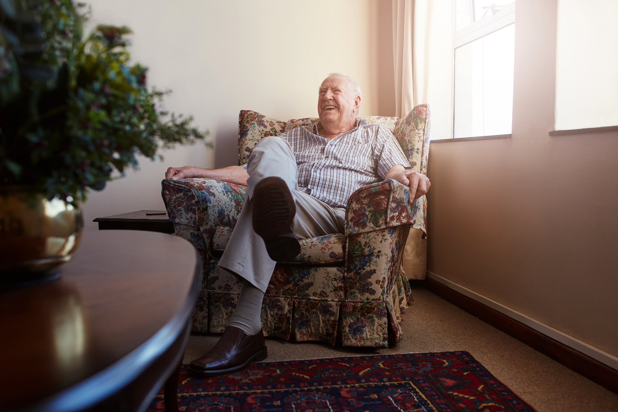 Senior man smiling and sitting in a chair in his retirement home room
