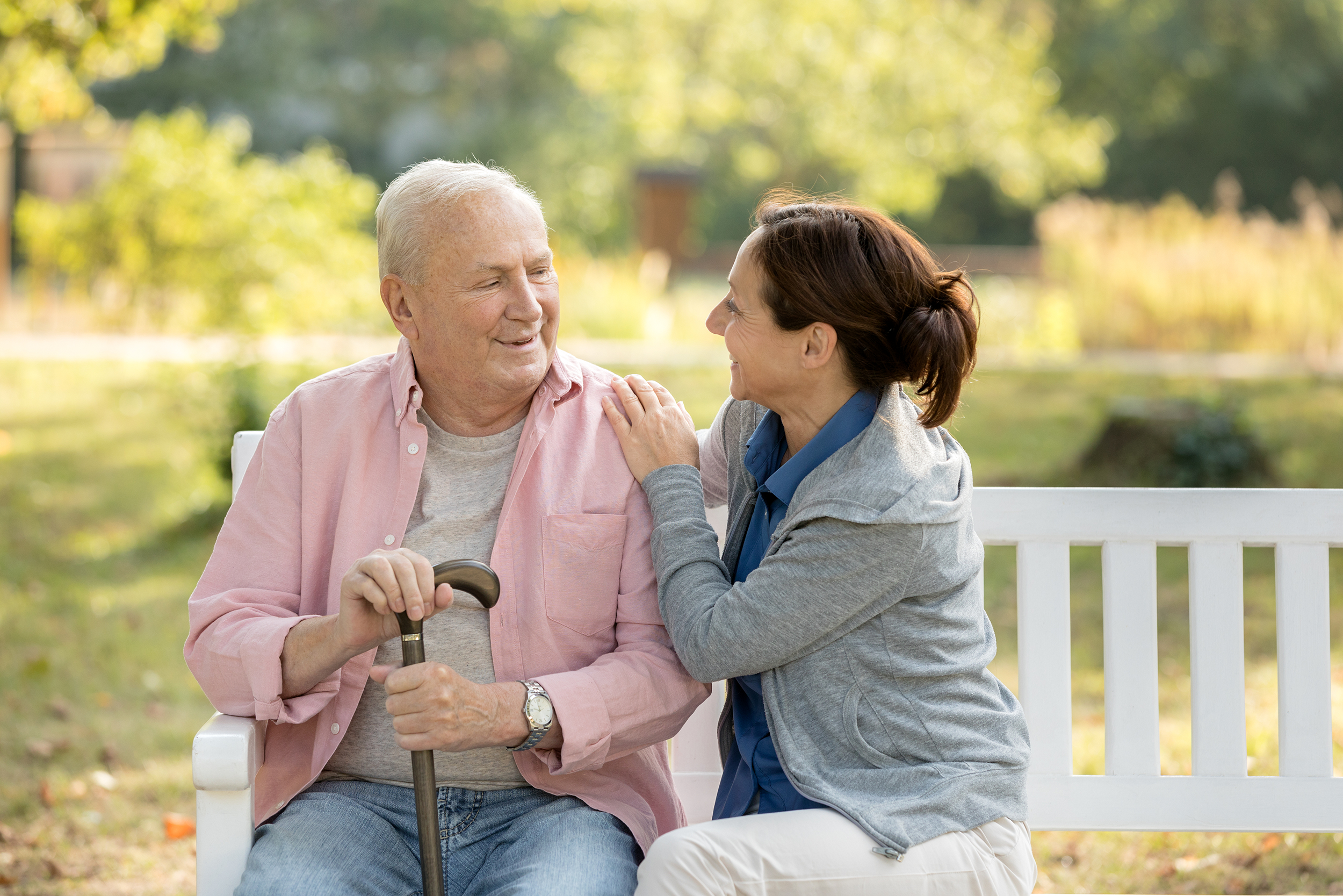 Senior living assistant speaking with a senior man on a bench outside