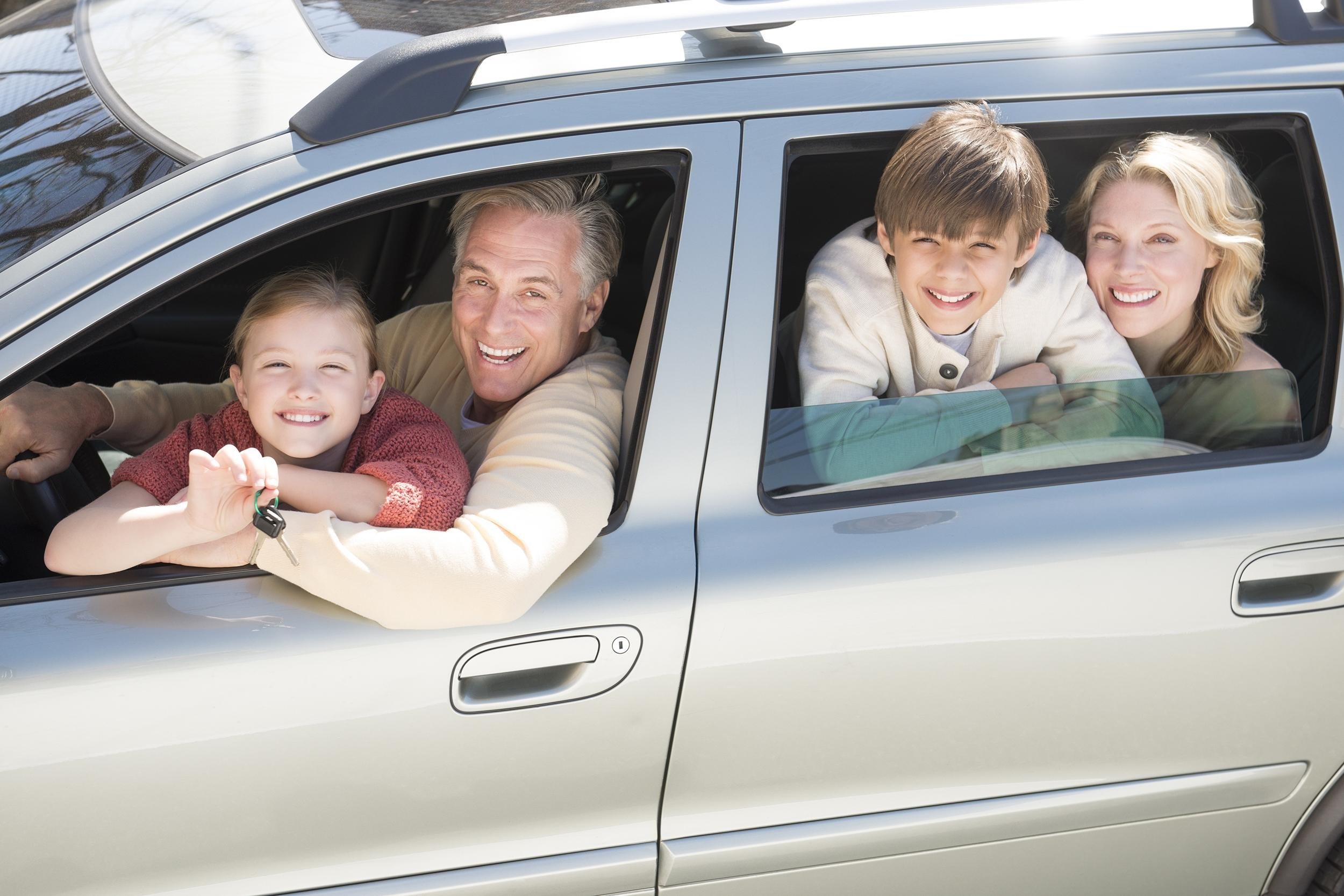 cheerful girl showing car keys while sitting with family in car