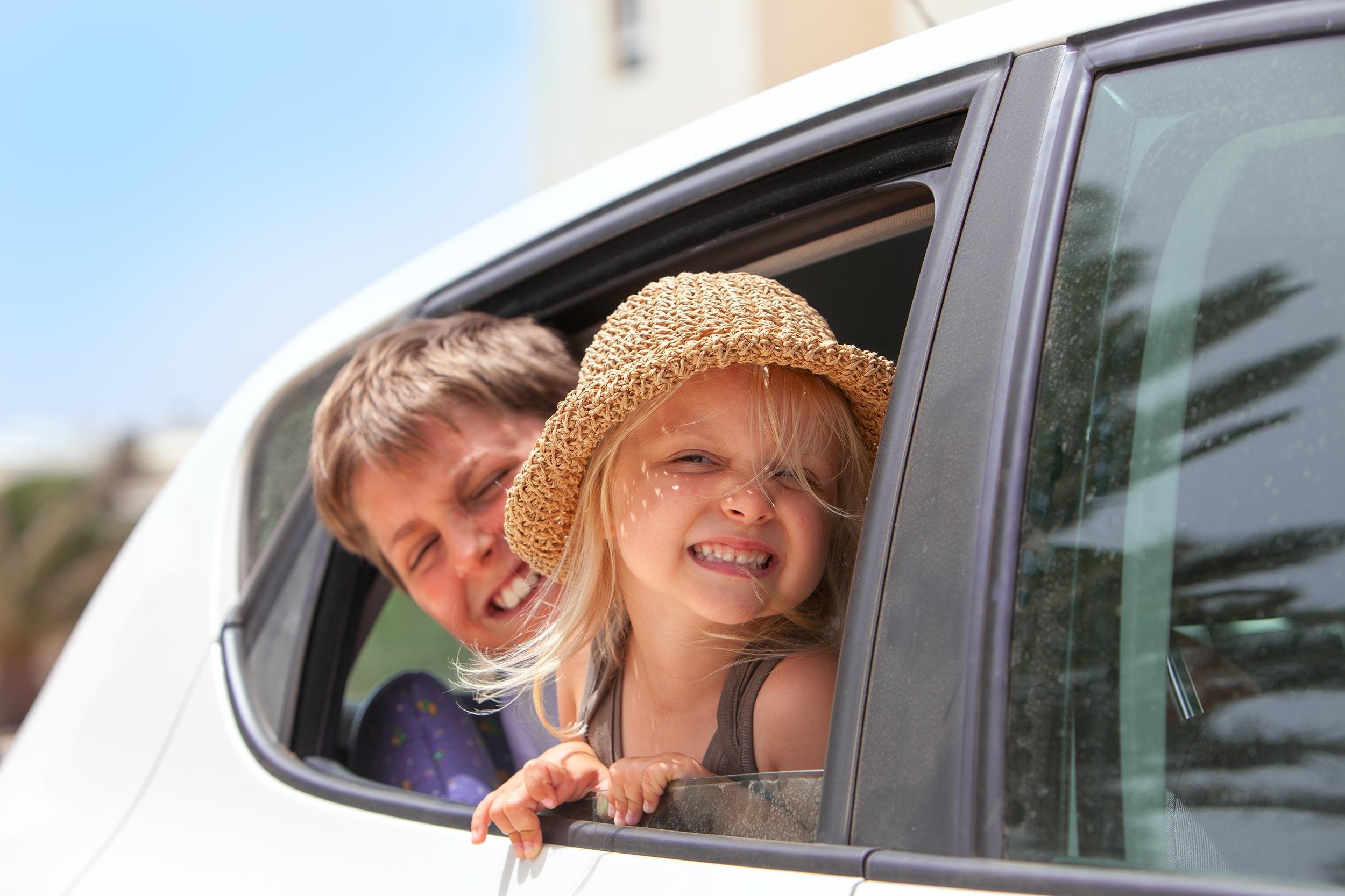 two happy kids hanging out of car window