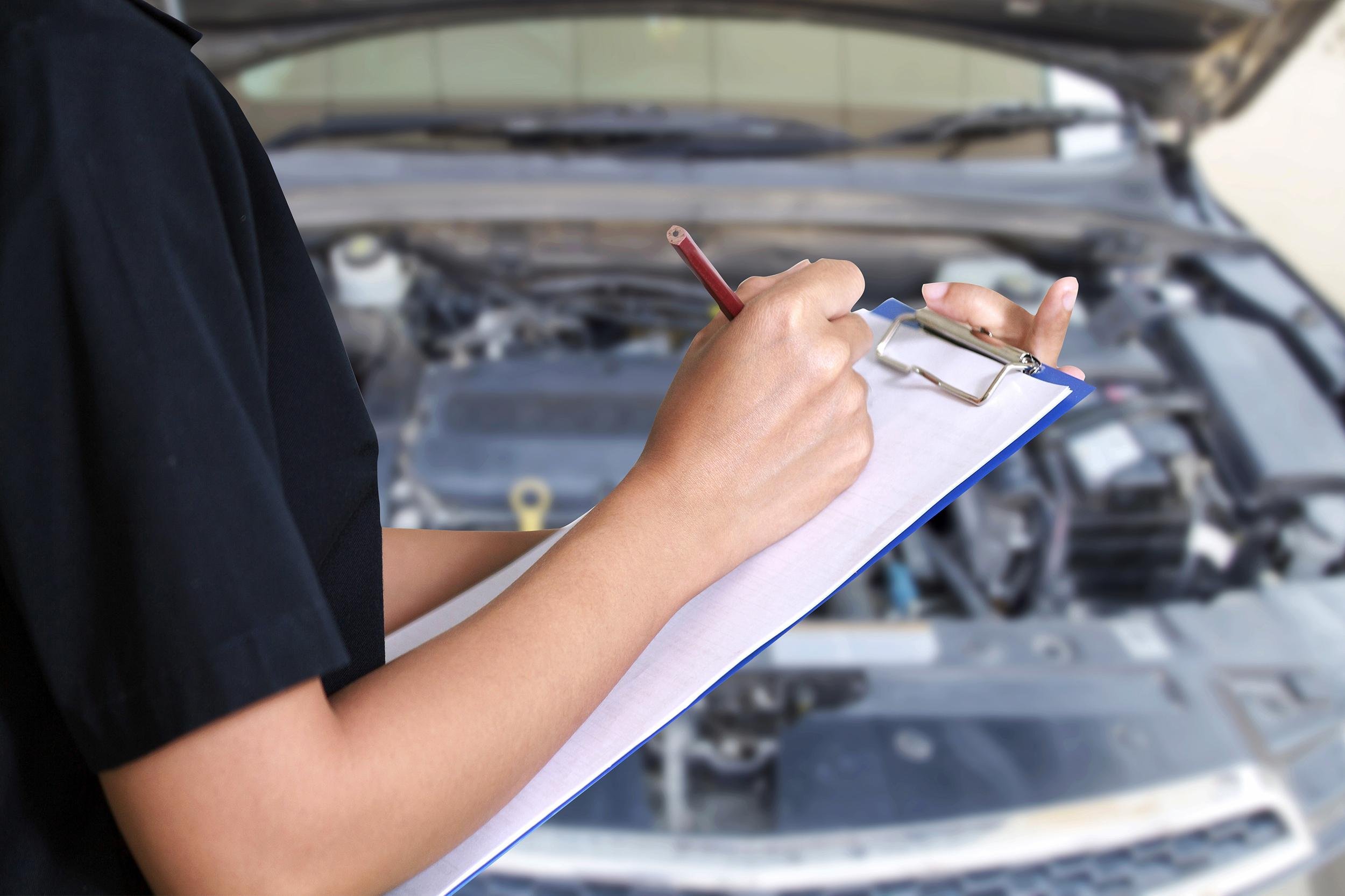 smiling young female mechanic inspecting on a car in auto repair shop