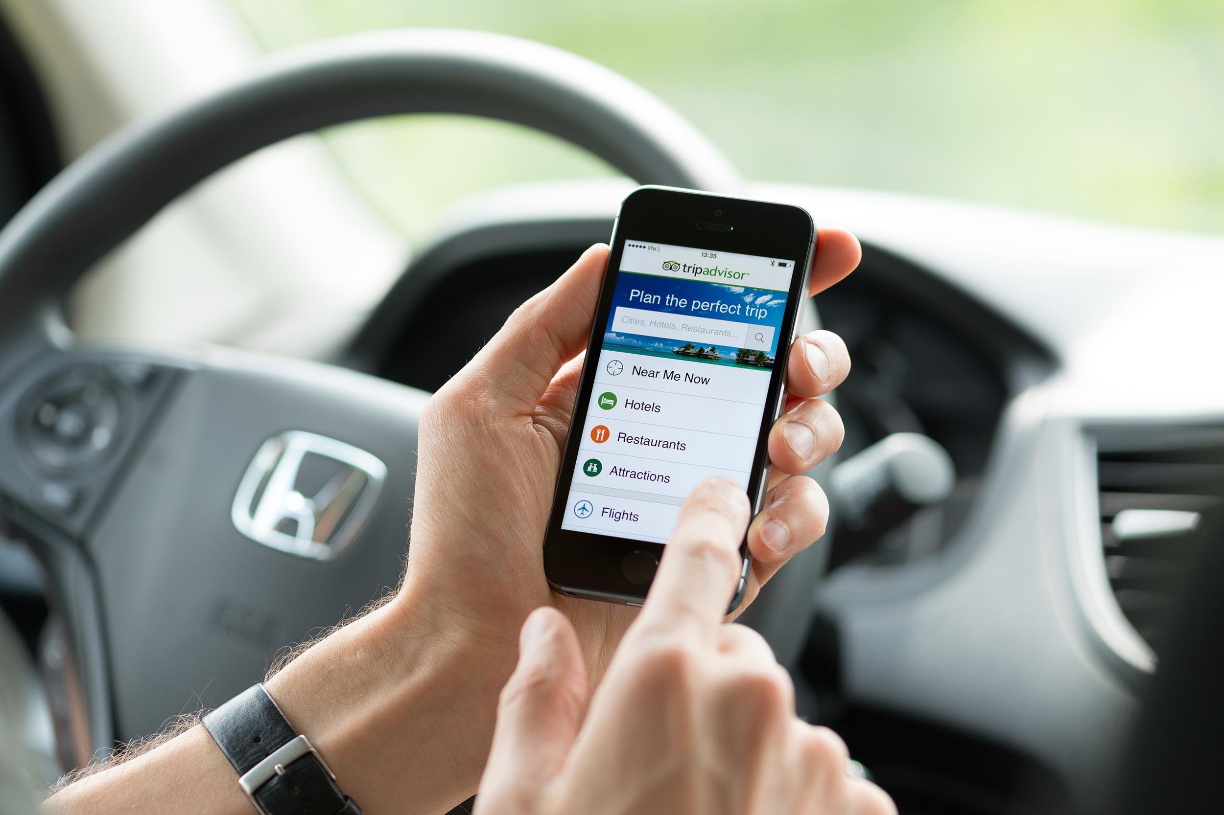 man in a car planning a trip using Tripadvisor app on Apple iPhone 5S