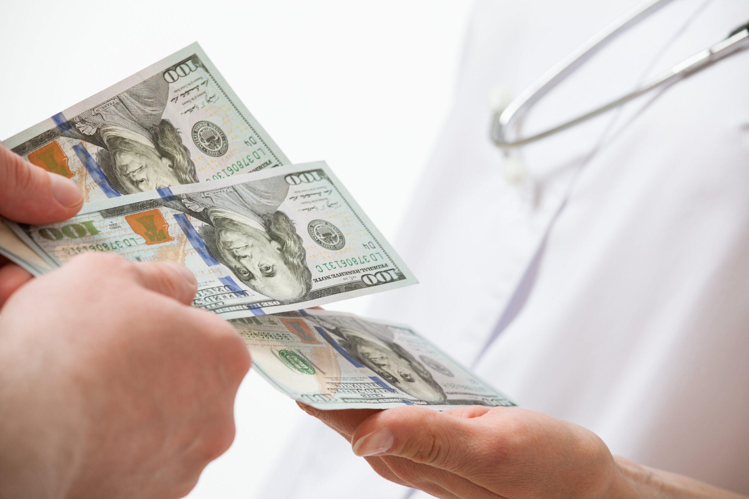 Doctor accepting payment in hundred dollar bills from a patient