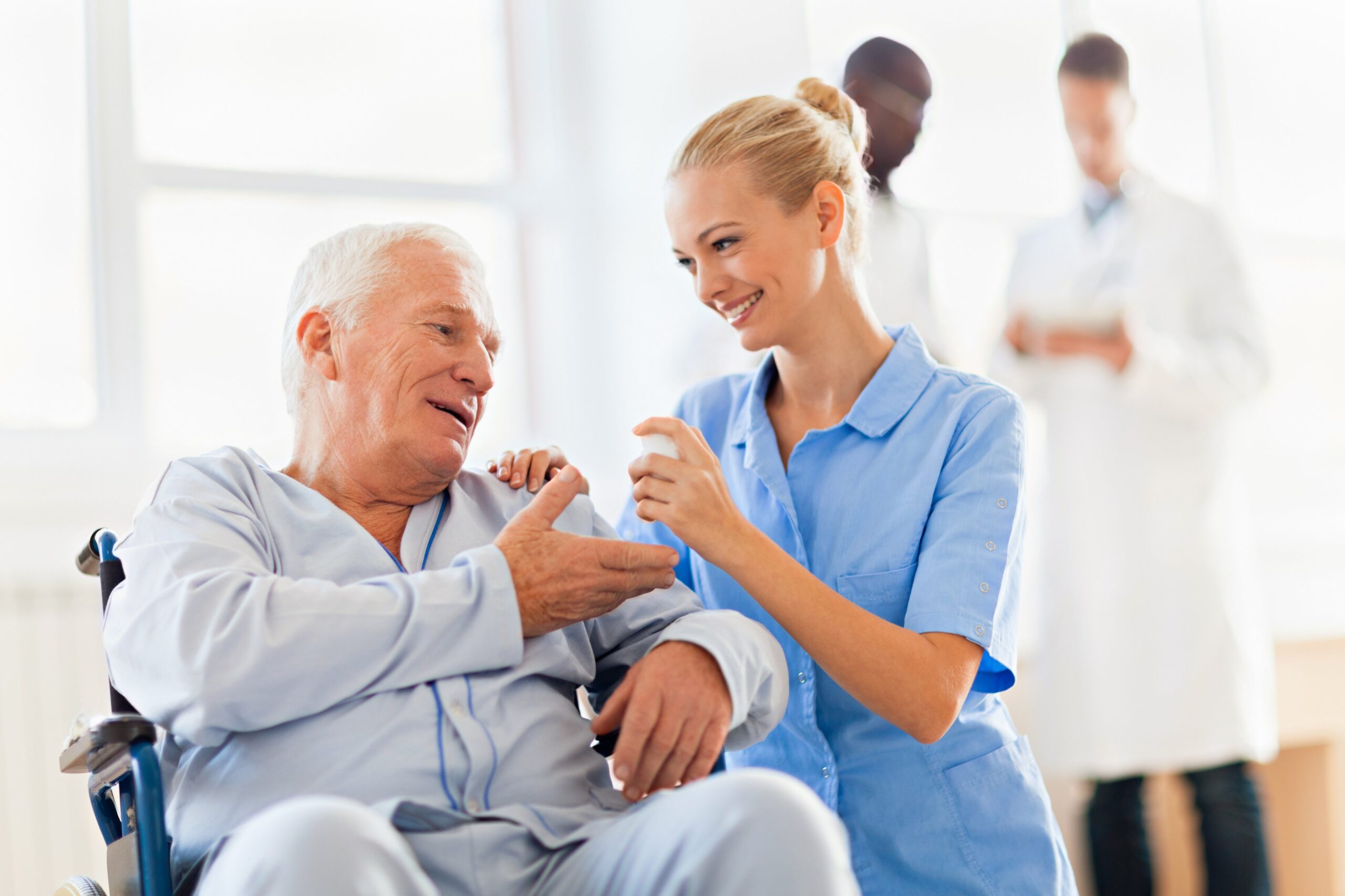 A nurse offers assistance to an elderly man in a wheelchair