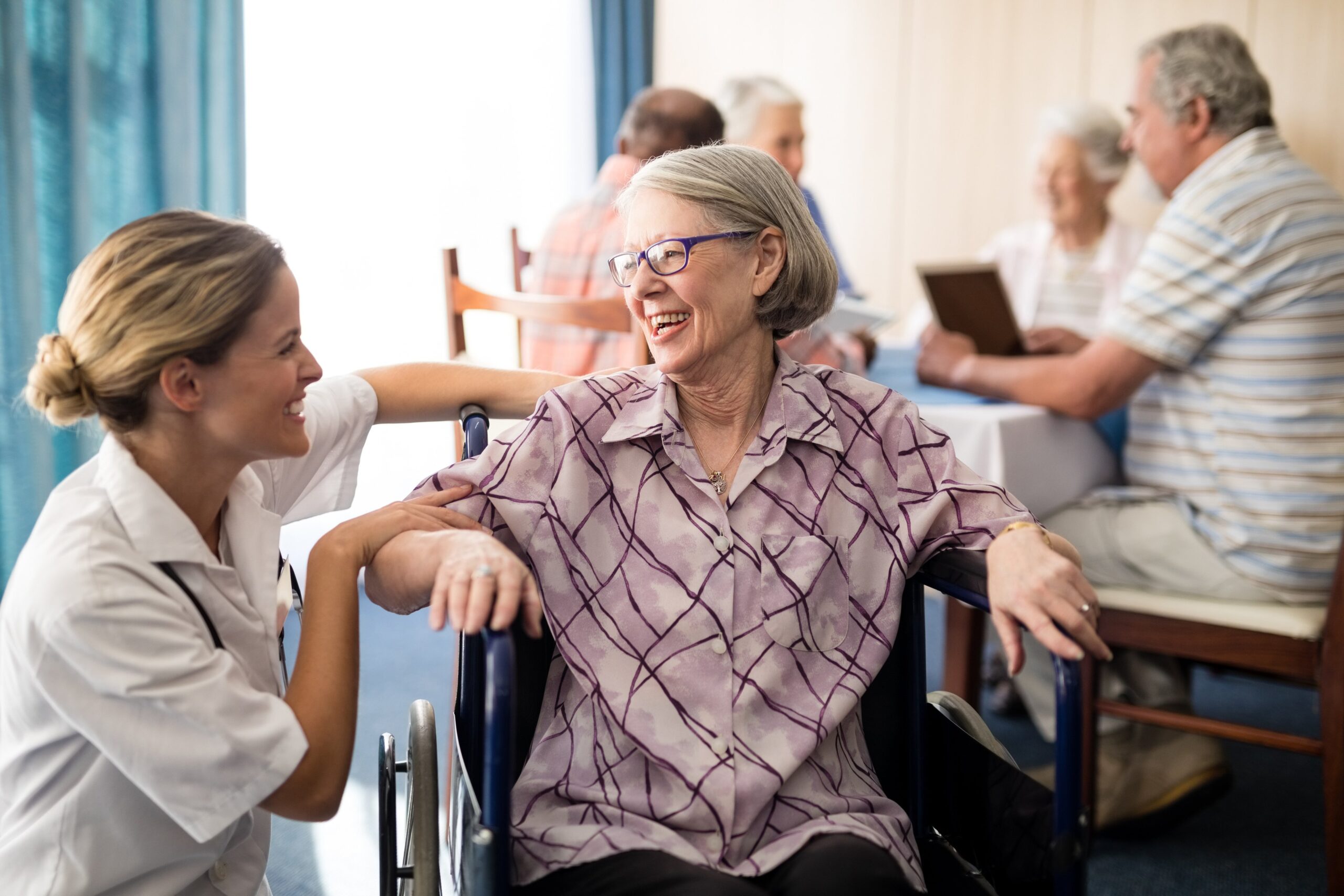 nurse attending to a cheerful elderly woman sitting in a wheelchair in a nursing home
