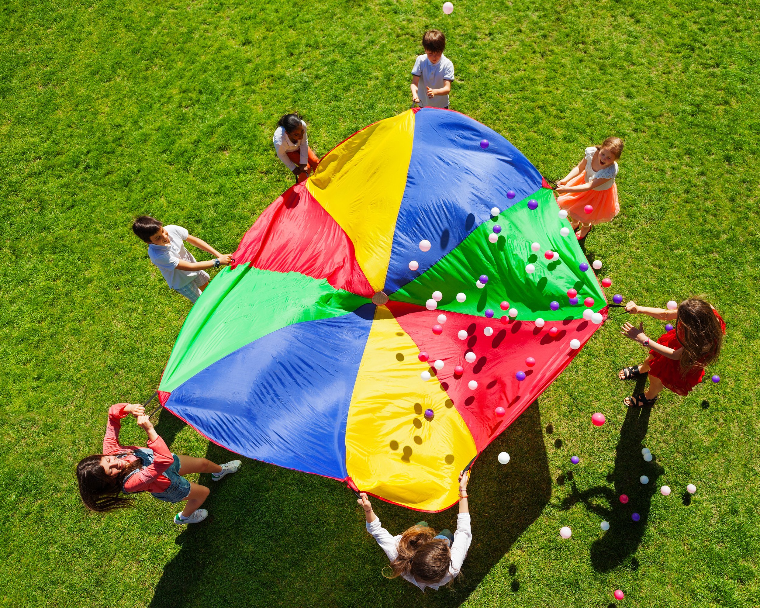 happy kids waving rainbow parachute full of balls