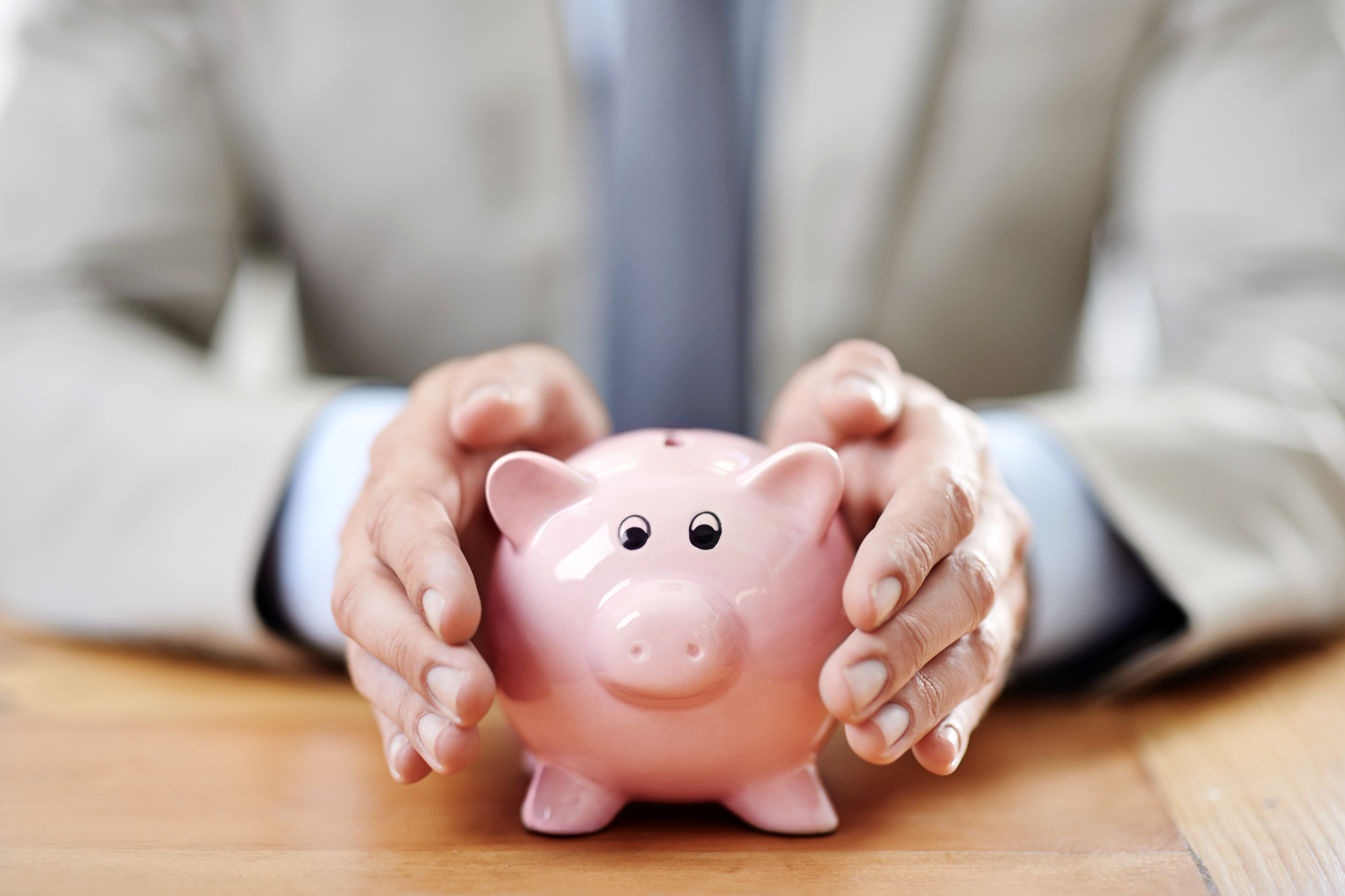 Business person cupping a piggy bank to protect it