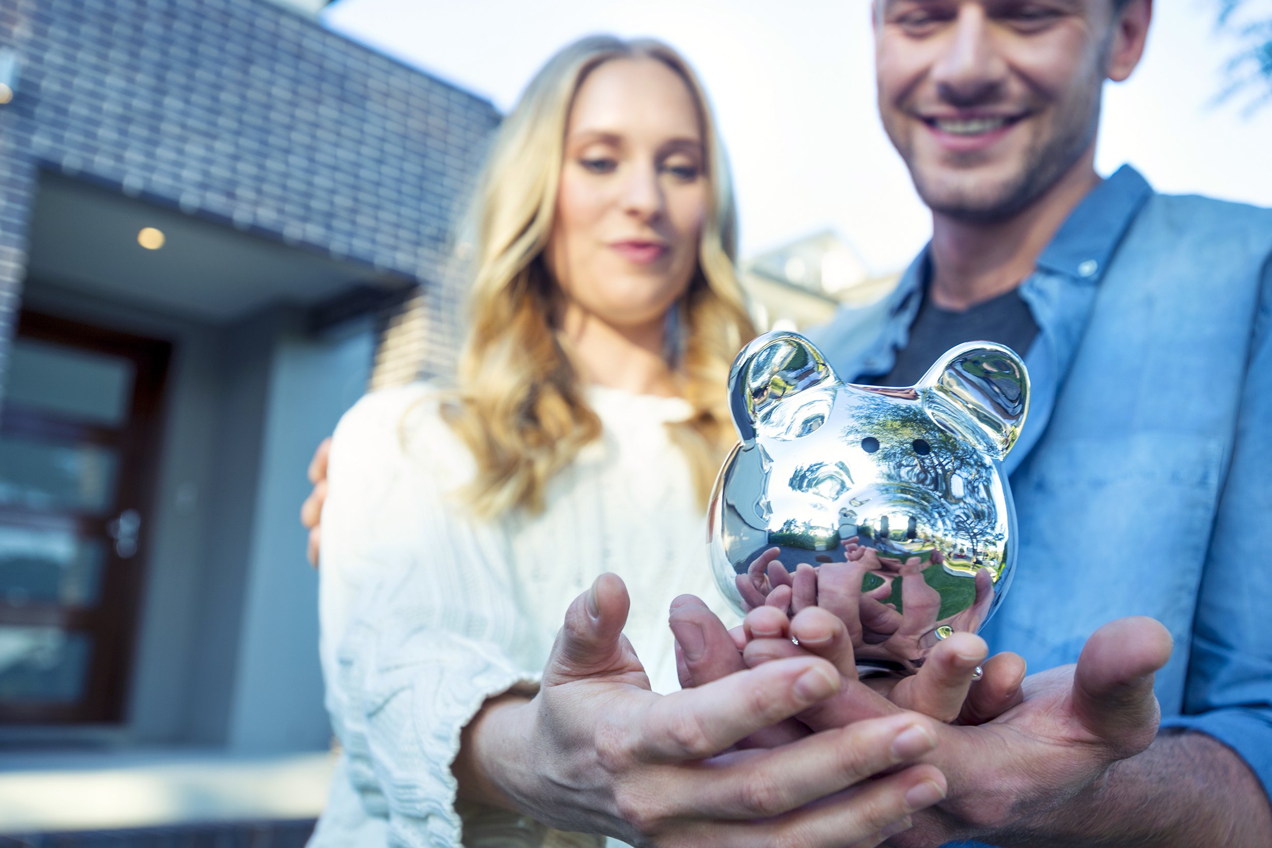 couple holding a piggy bank in front of house