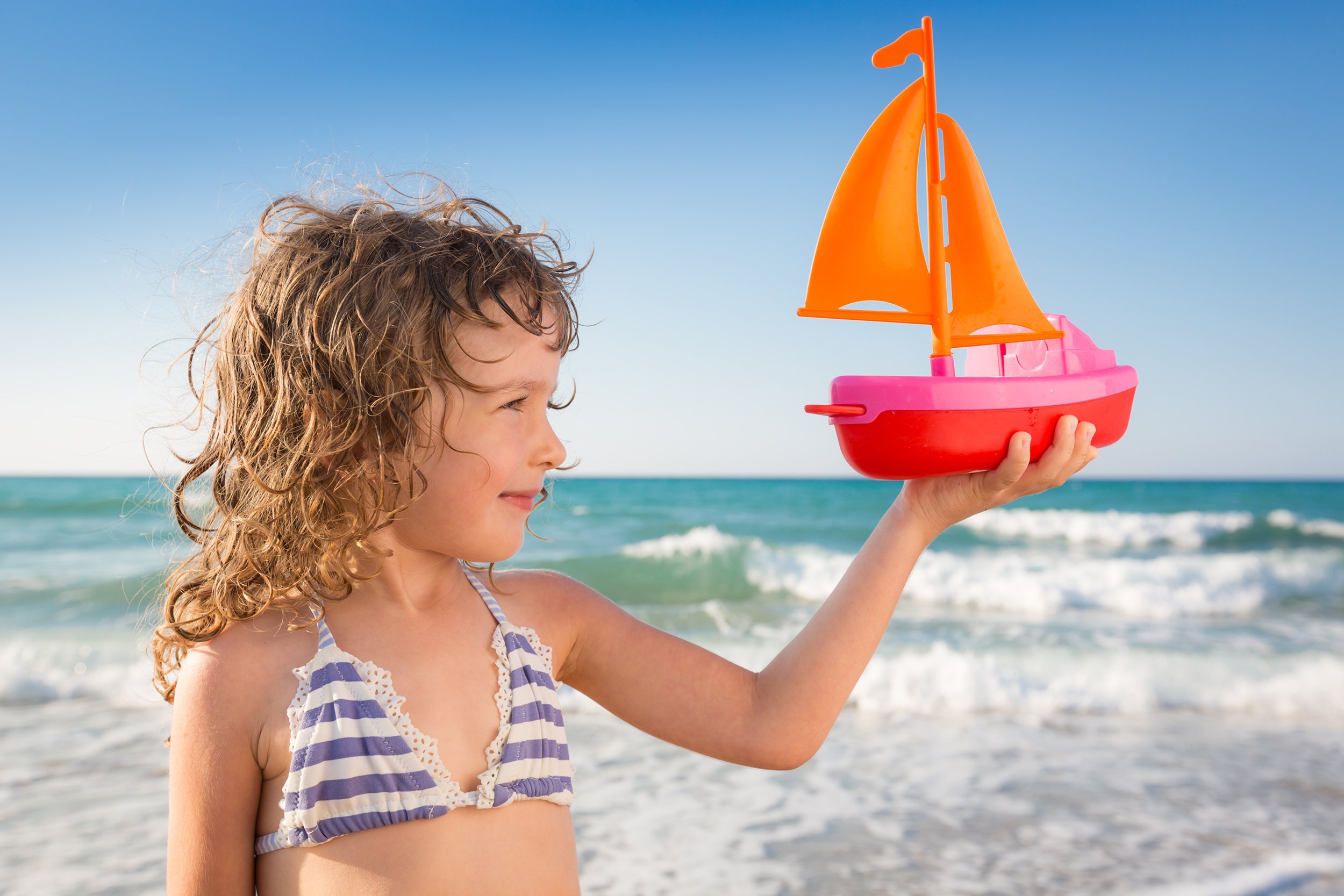 happy child playing with toy sailing boat against blue sea and sky