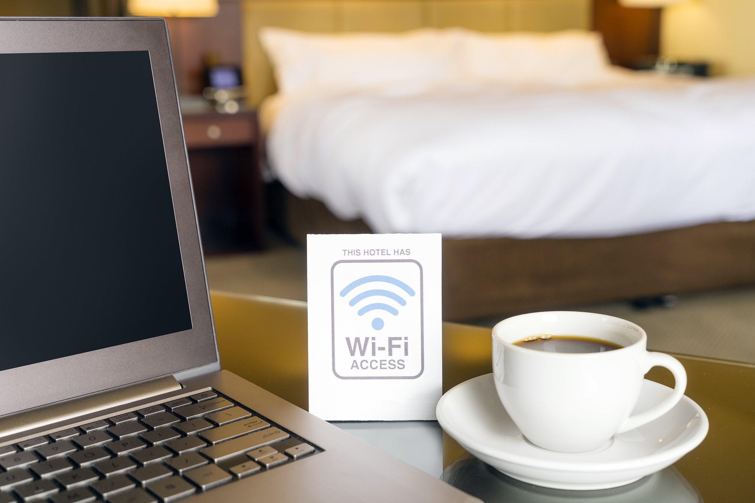hotel room with wifi access sign, laptop, and cup of coffee