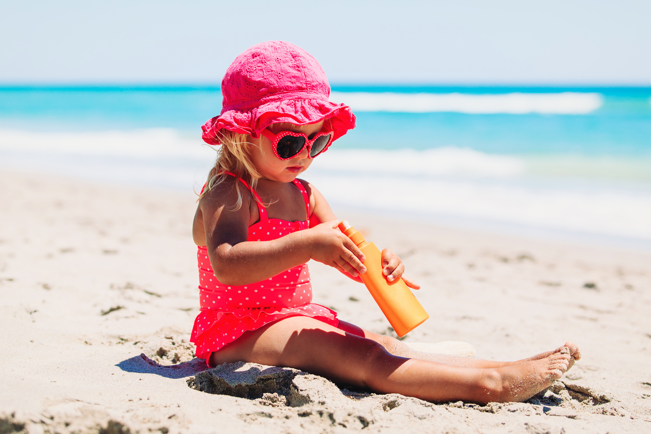 Young girl sitting on the beach applying sunscreen