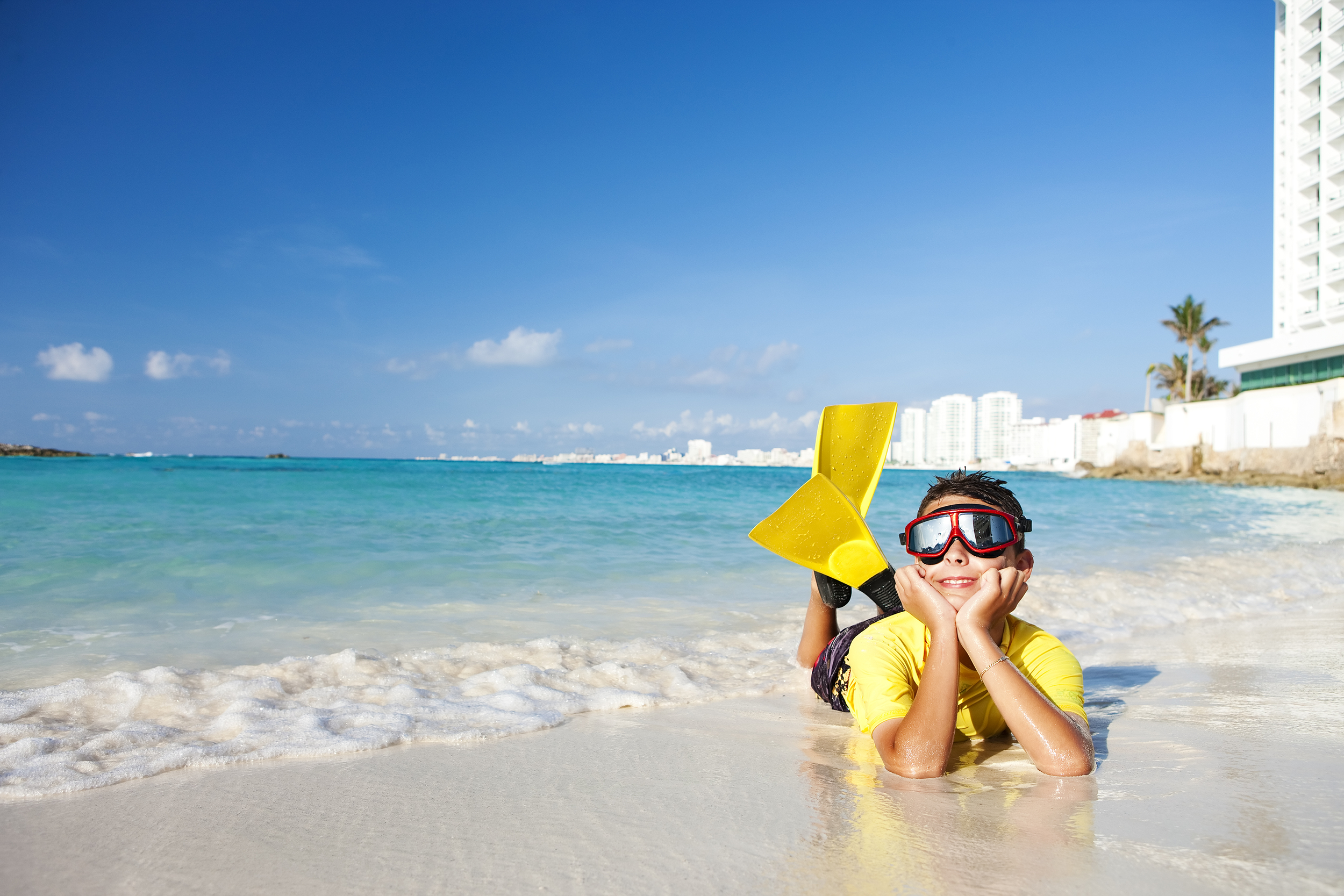 Young boy wearing scuba flippers lying on the beach in Mexico