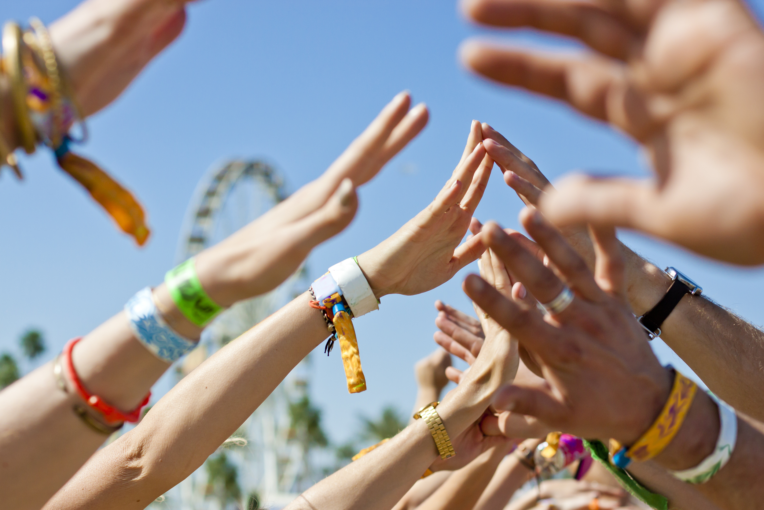 Hands with wristbands at a festival reaching toward the sky