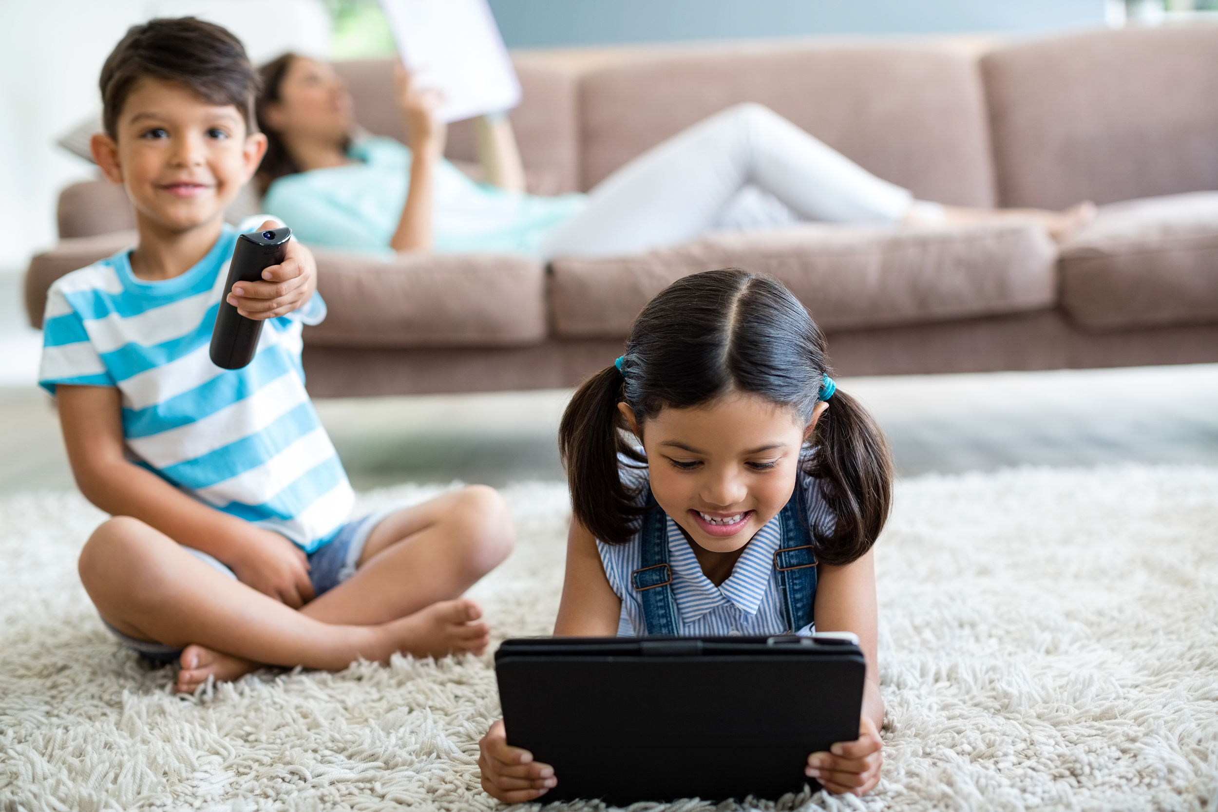 Brother and sister watching tv and playing on a tablet