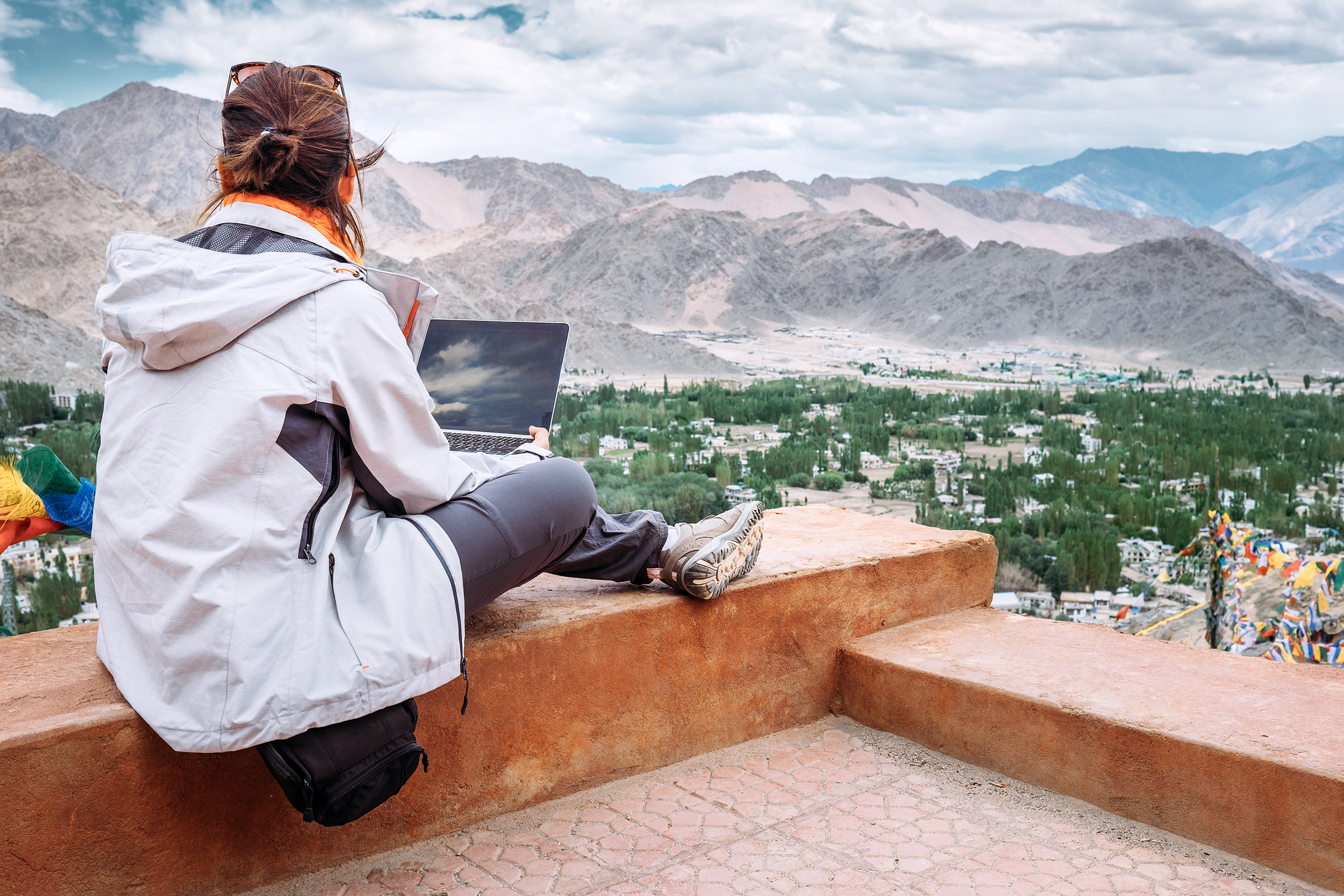 Woman sitting on a rooftop with her laptop looking at the mountains and city