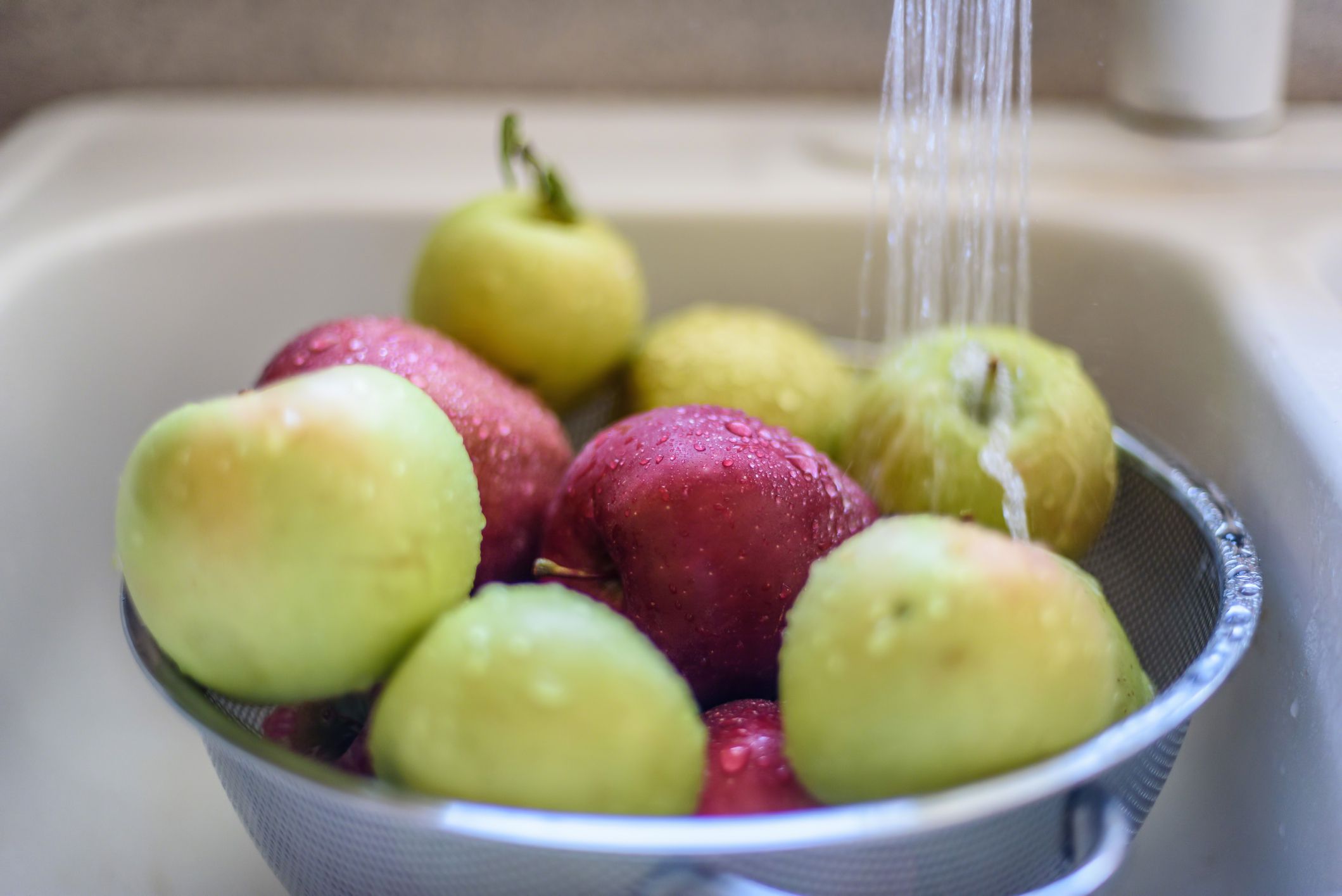 Washing red and green apples in strainer in sink, water is running