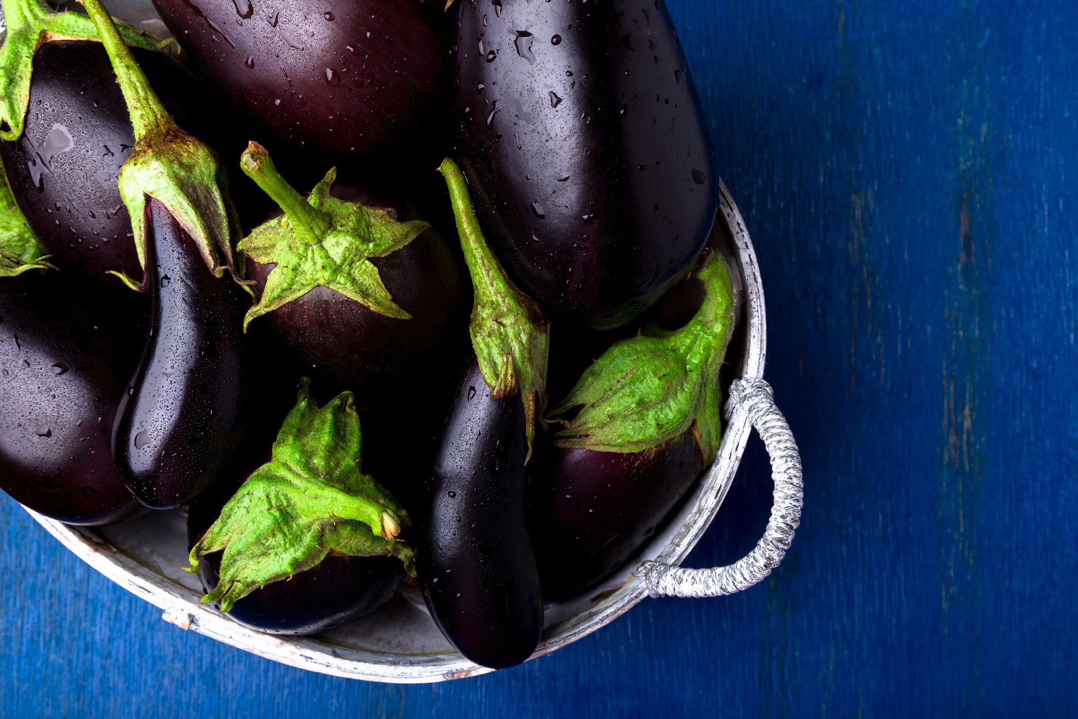 Fresh eggplant in grey basket on blue wooden table.Rustic background. Top view. Copy space. Vegan vegetable