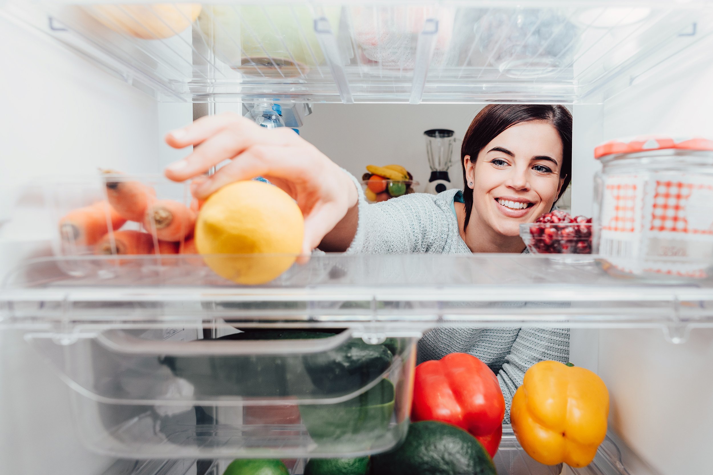 smiling woman taking a fresh lemon out of the fridge