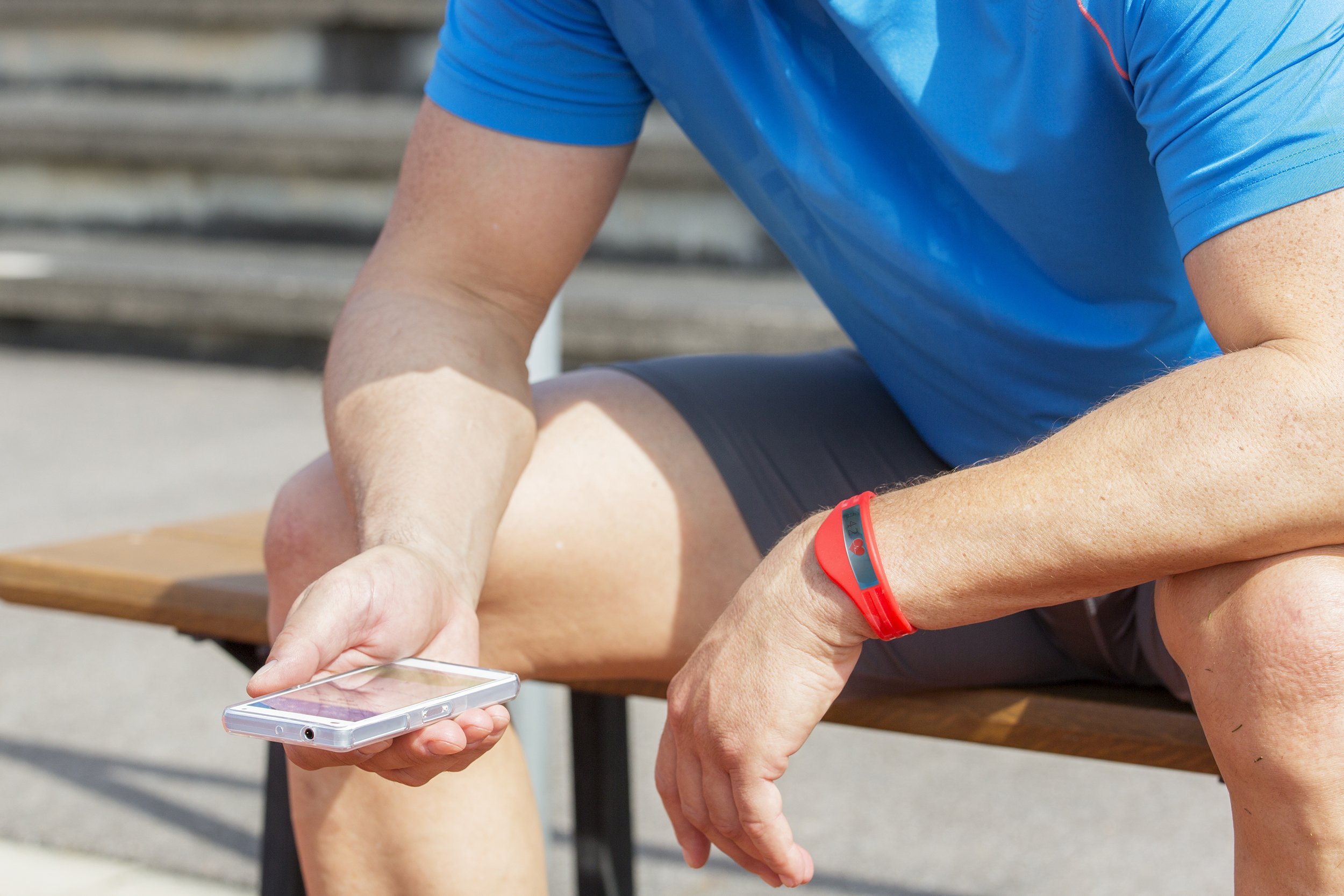 man sits on a bench and checks his fitness results on a smart phone