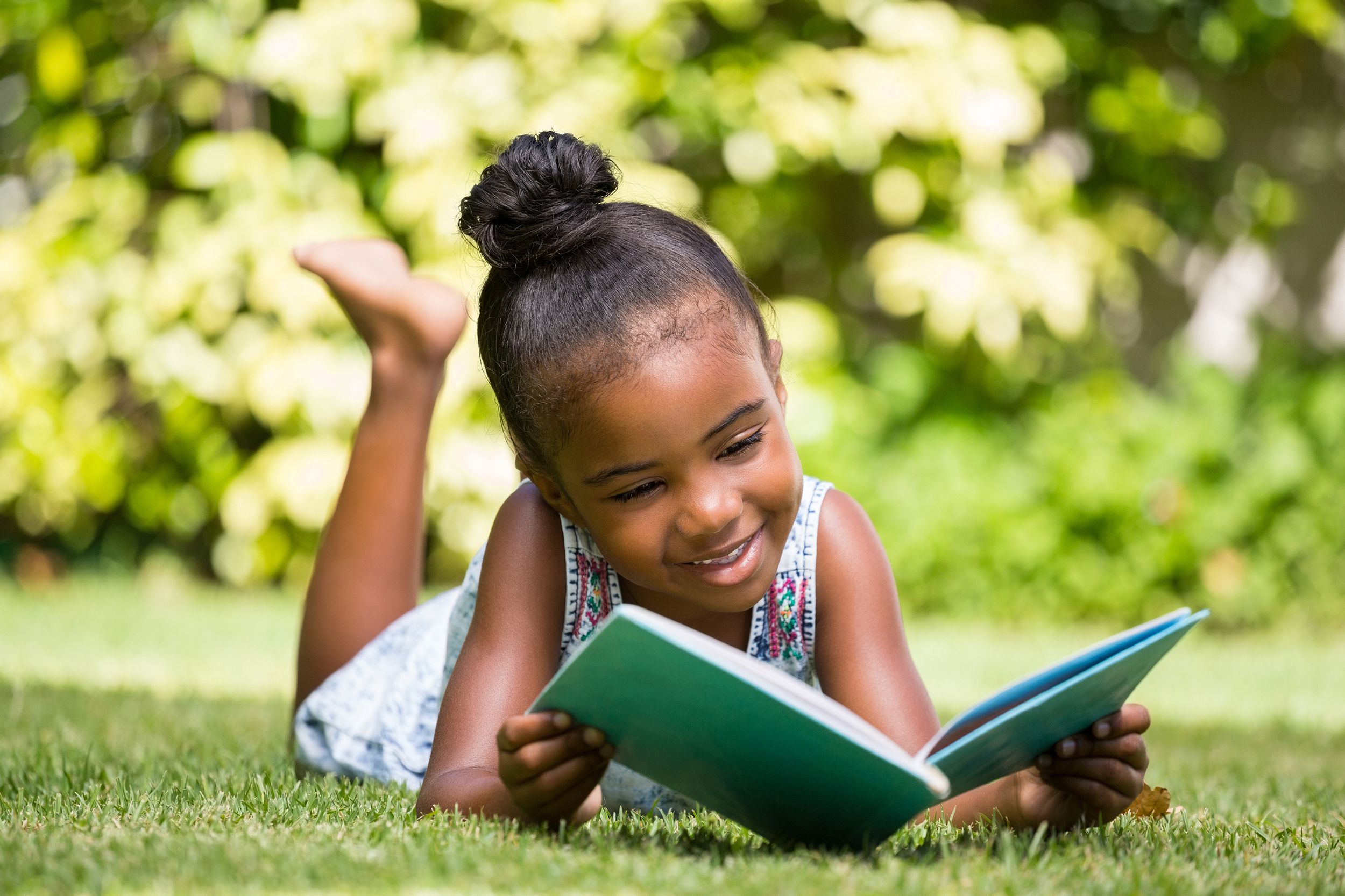 Little girl reading a book outside on the grass