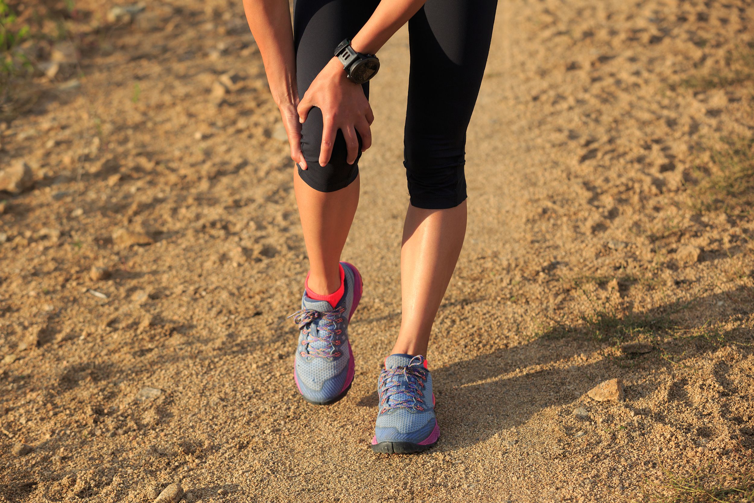 woman runner hold her sports injured knee on dirt road
