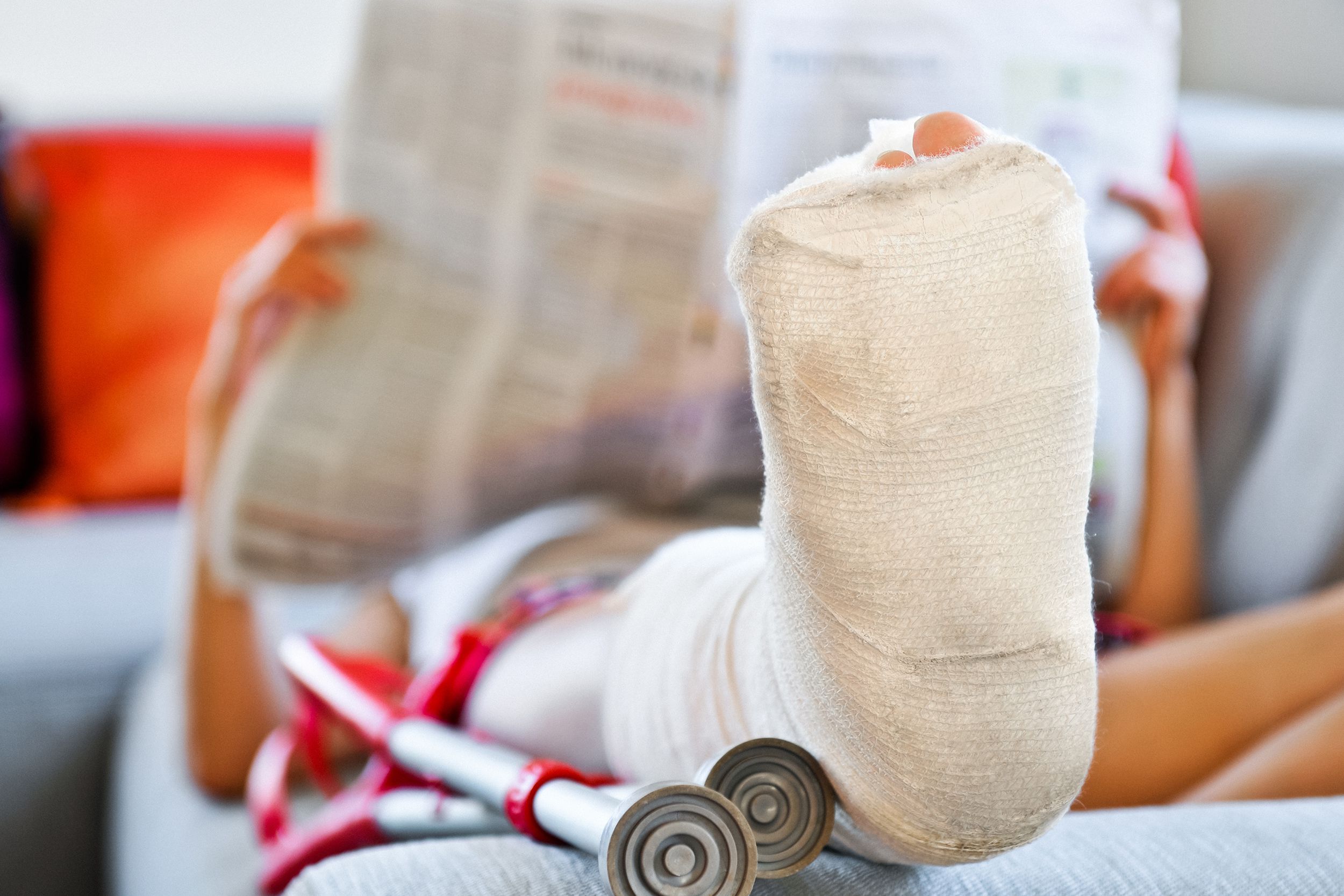 woman with broken leg lying on sofa and reading newspaper