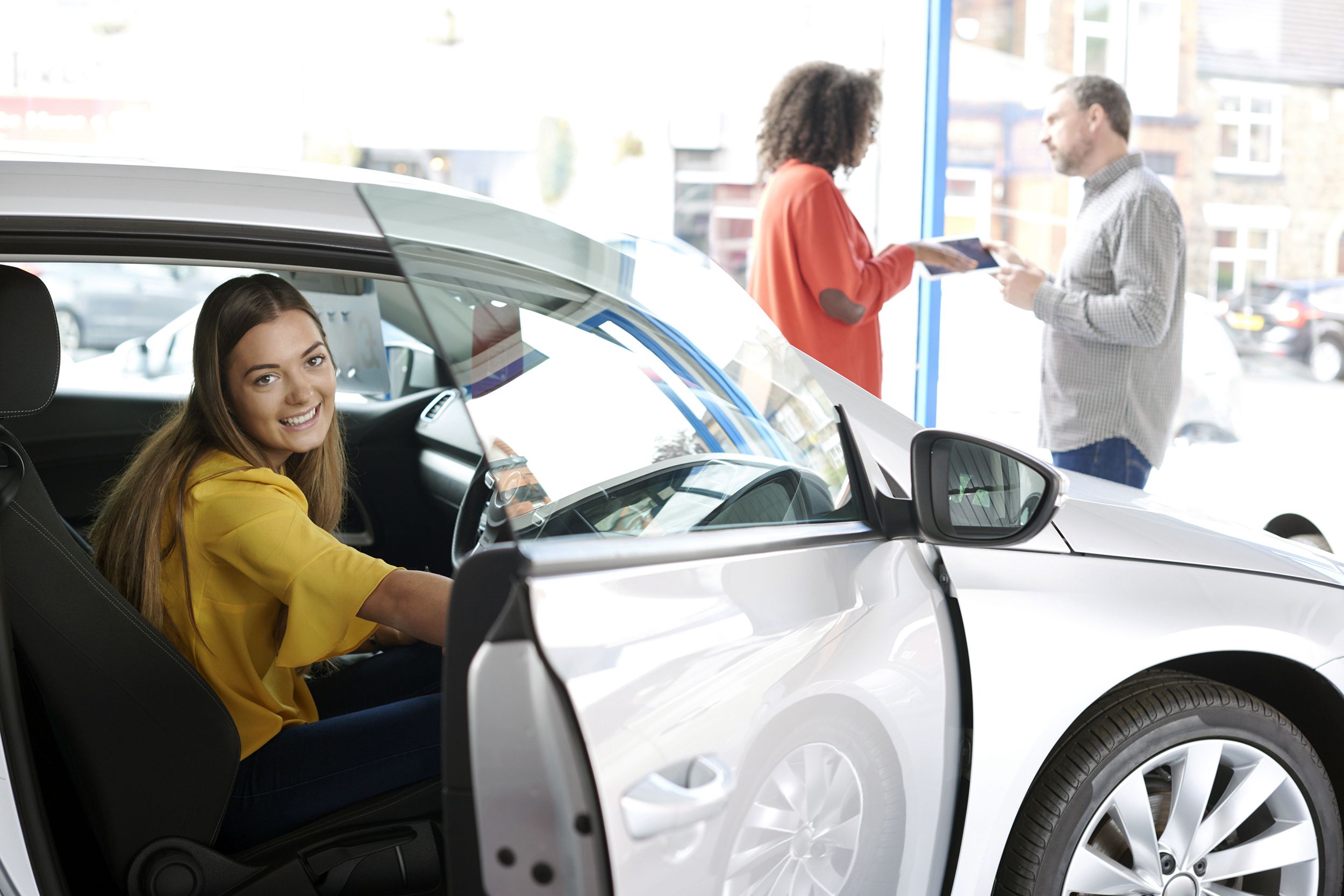 teenager in car at dealership with parent and salesperson in background