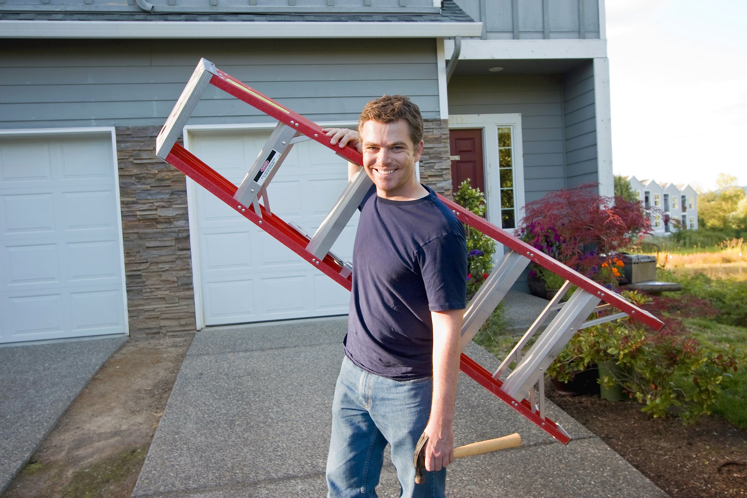 Man carrying a ladder in front of his house