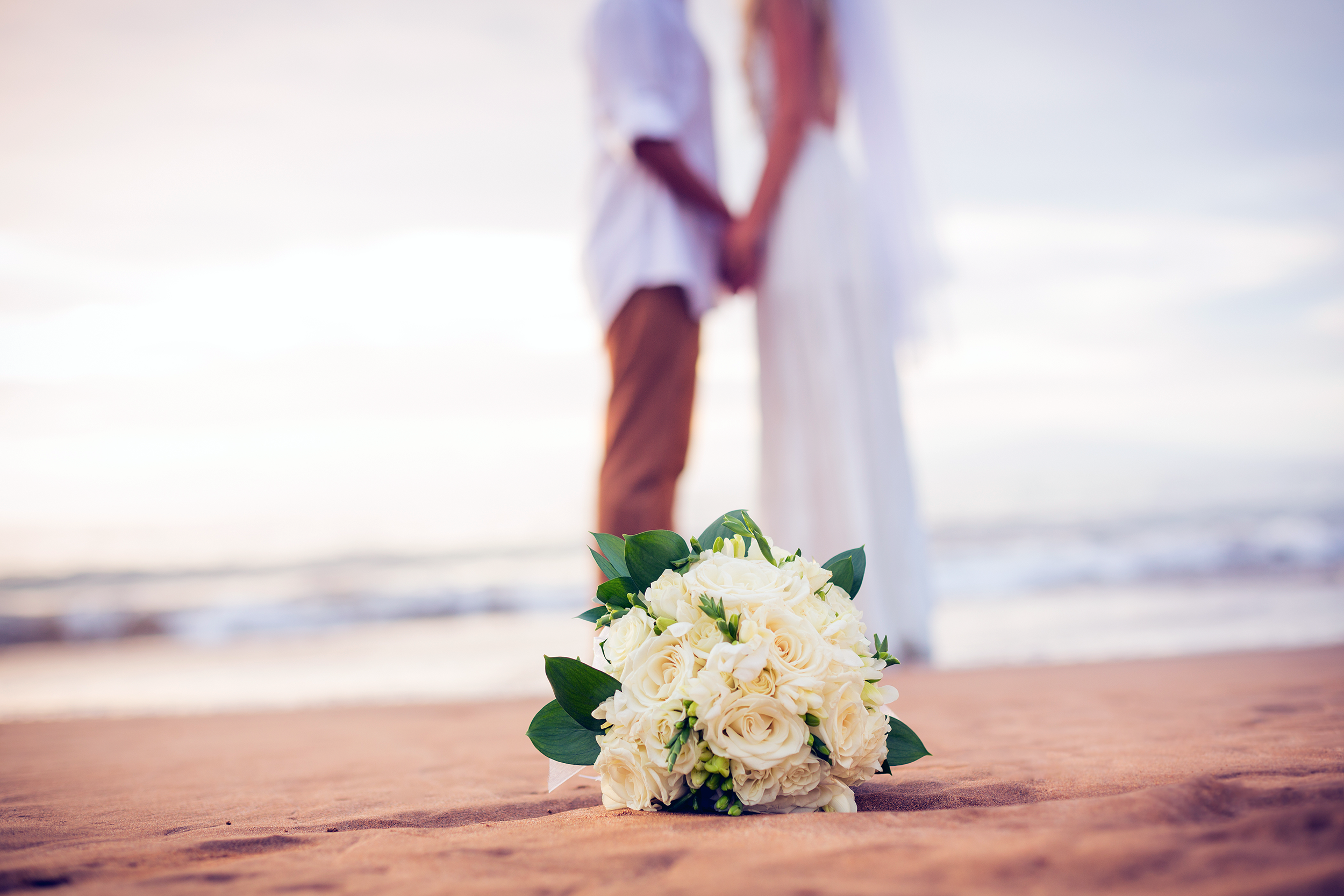 Wedding flower bouquet on the beach with couple in the background with the ocean