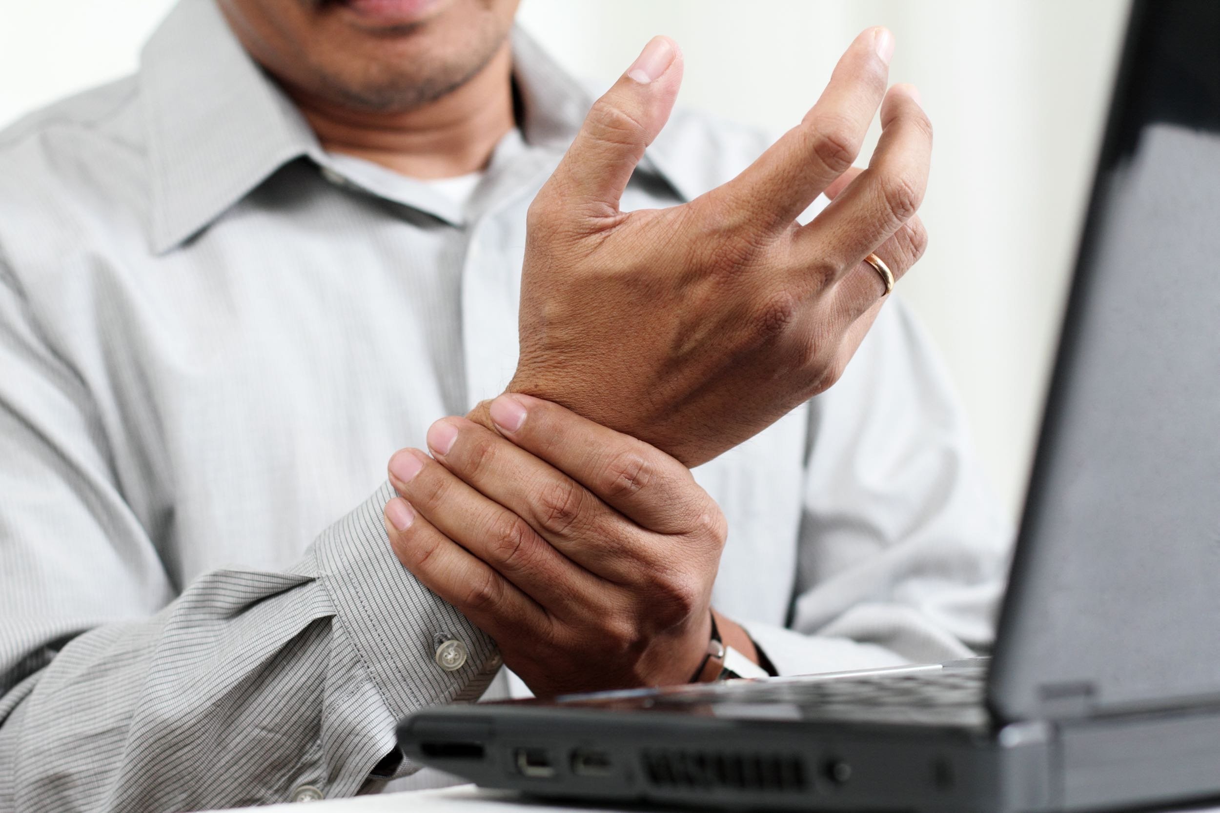 man at laptop holding pain in wrist