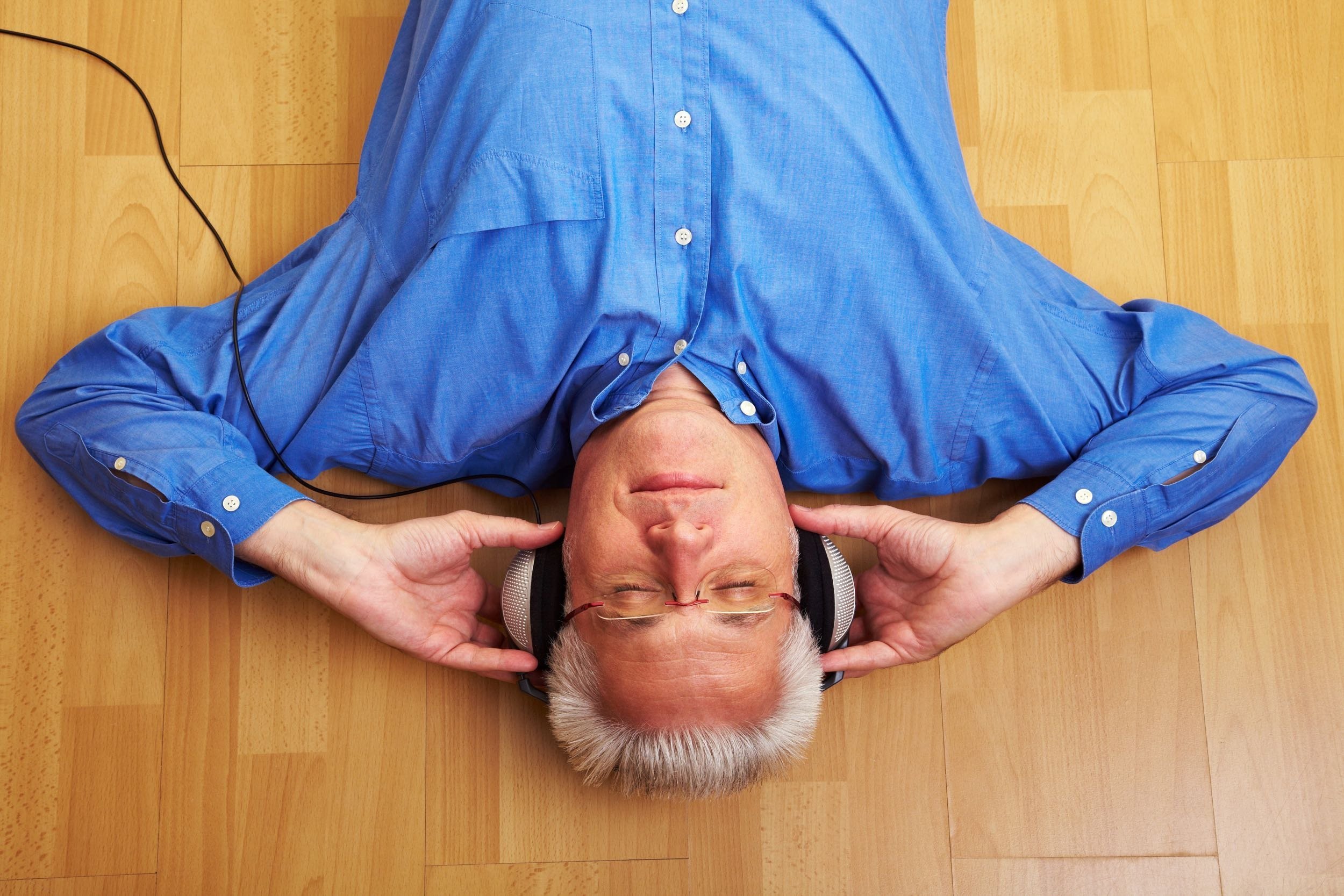 middle-aged man laying down on the floor listening to music with headphones