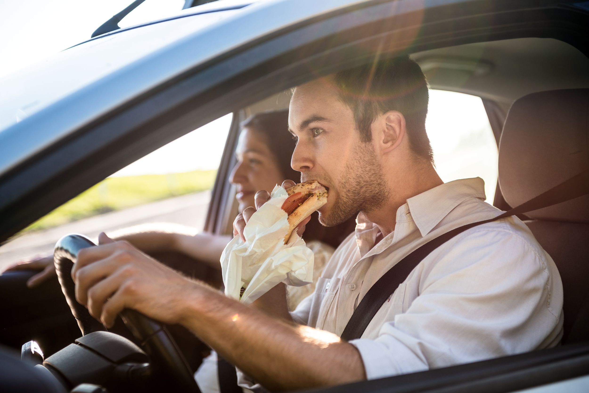 man eating sandwich while driving car