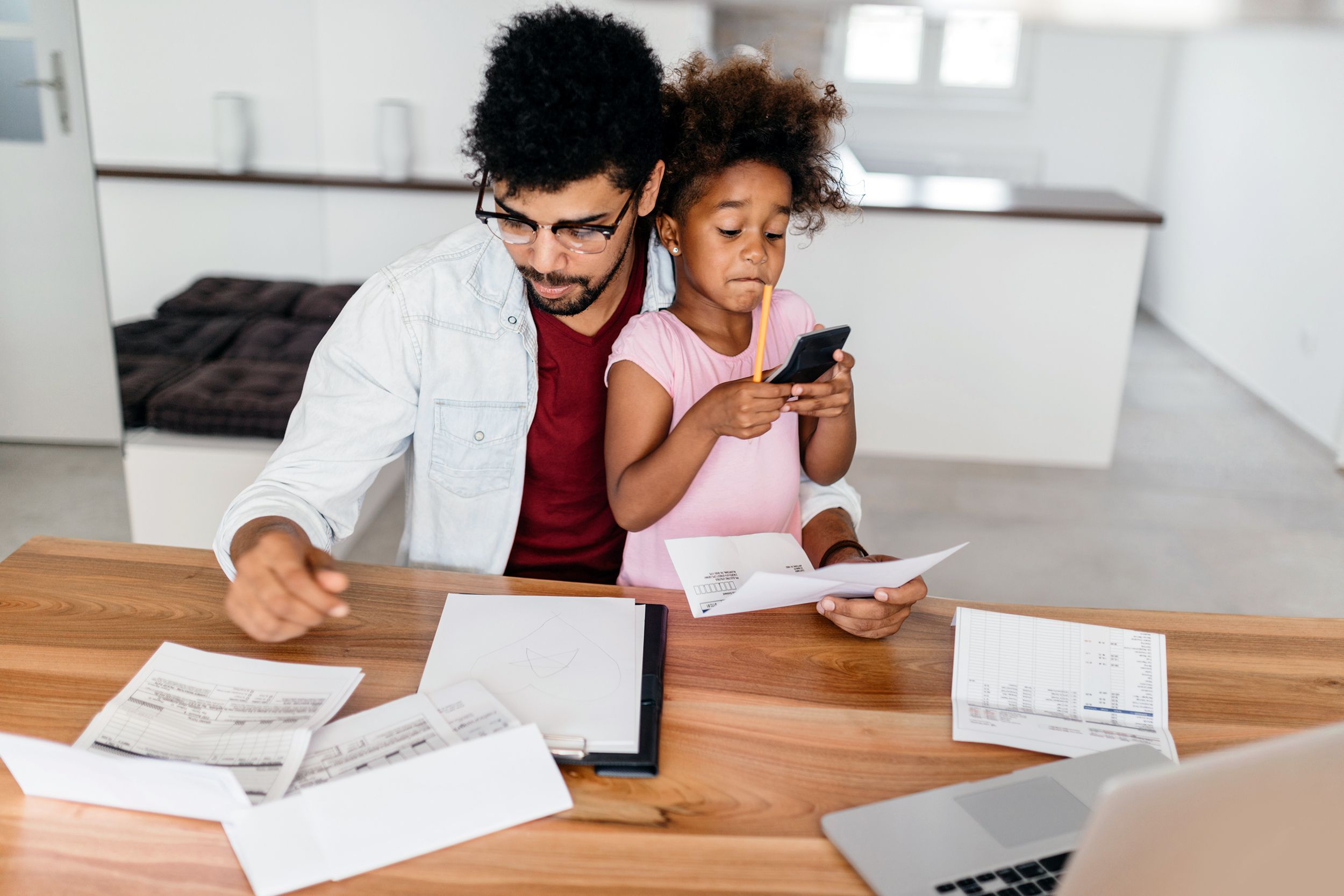 father looking bills while child is sitting in his lap and she is using calculator