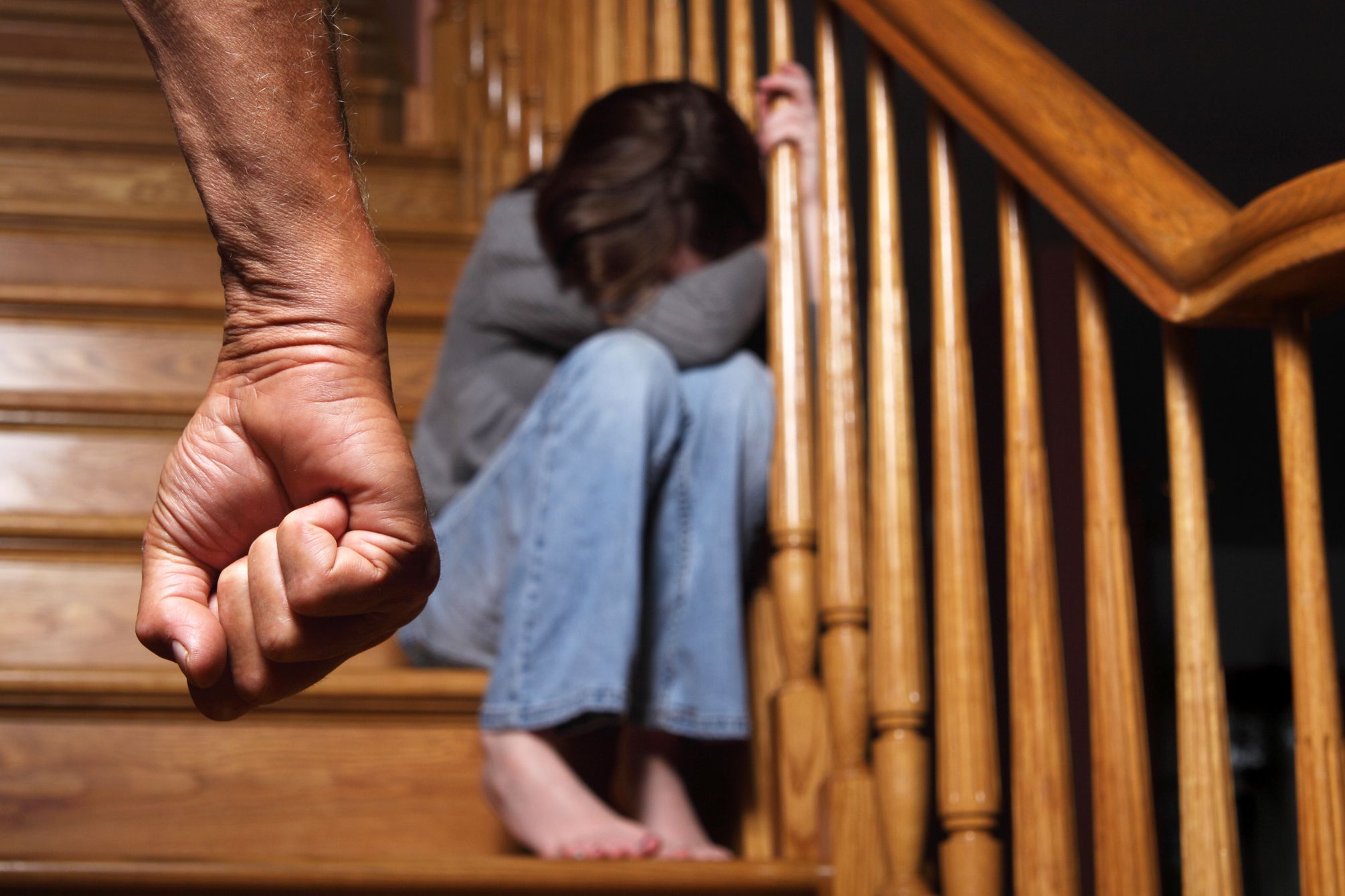 threatening fist in front of child with head down sitting on staircase