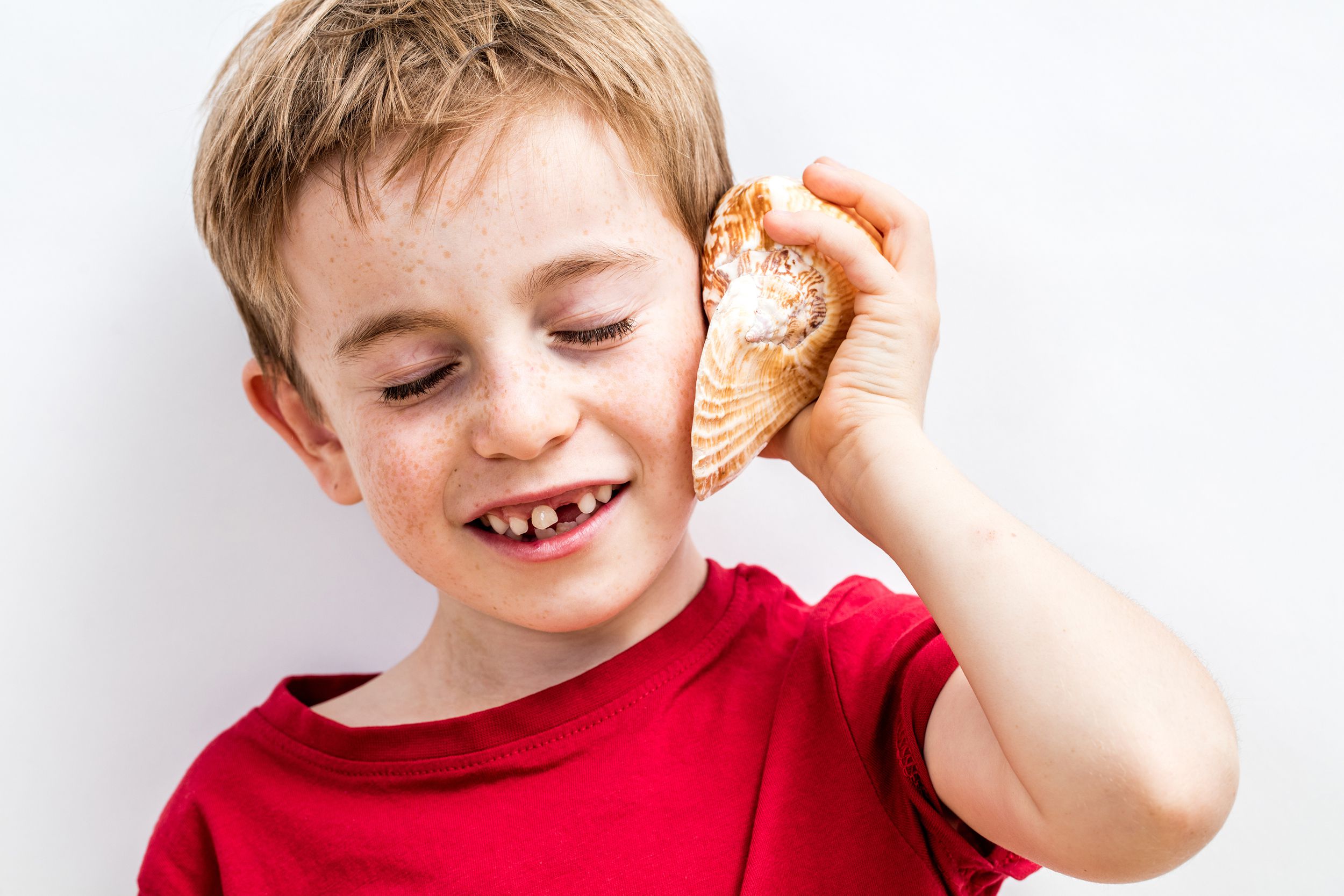 smiling imaginative beautiful child listening to ocean on a shell