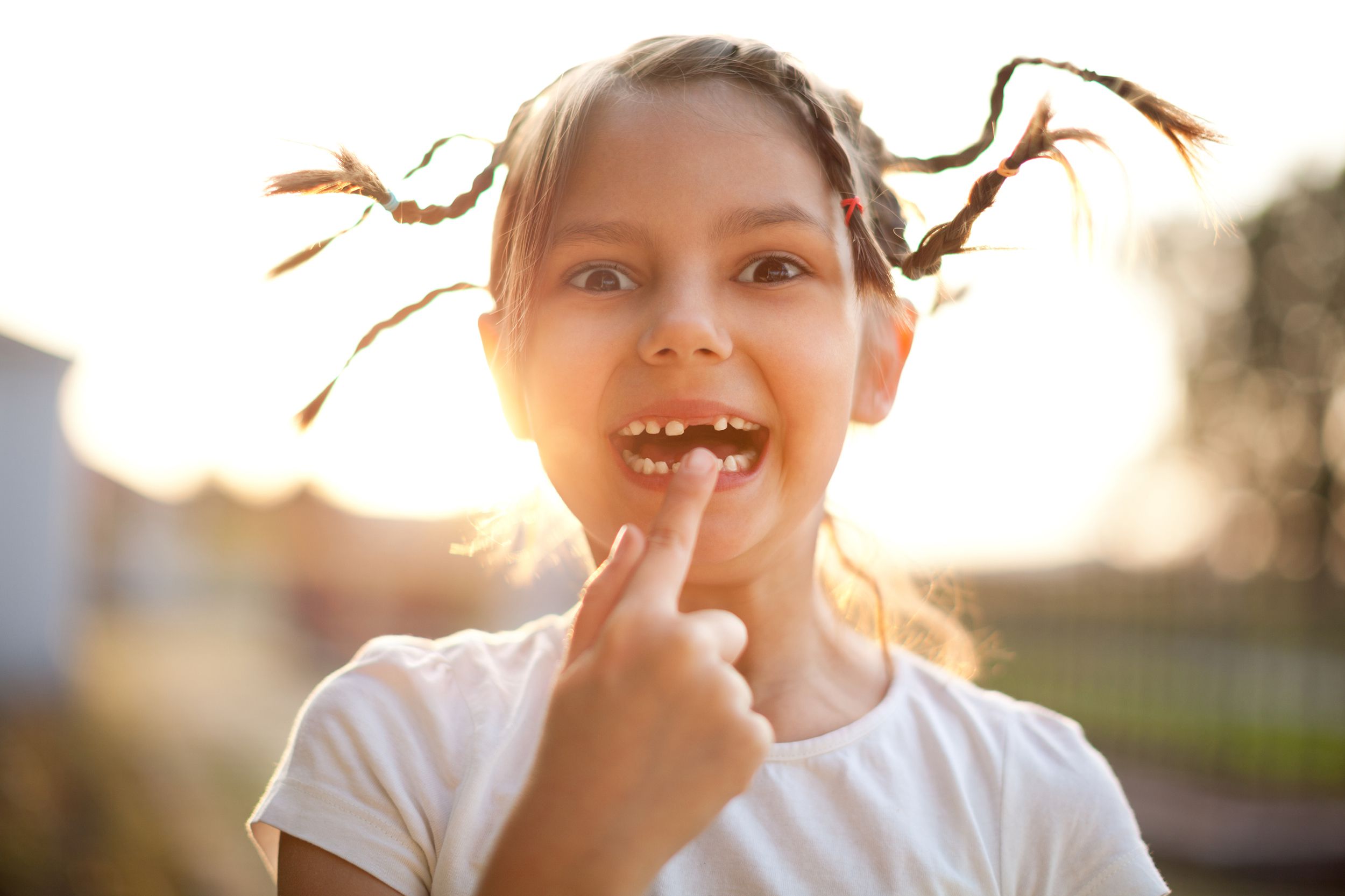 little girl with pigtails outdoors, pointing to her missing tooth