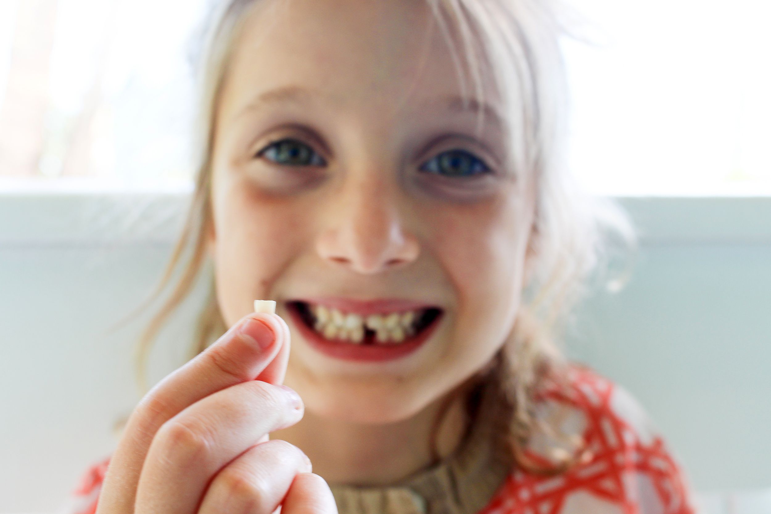 little girl holding lost tooth while smiling