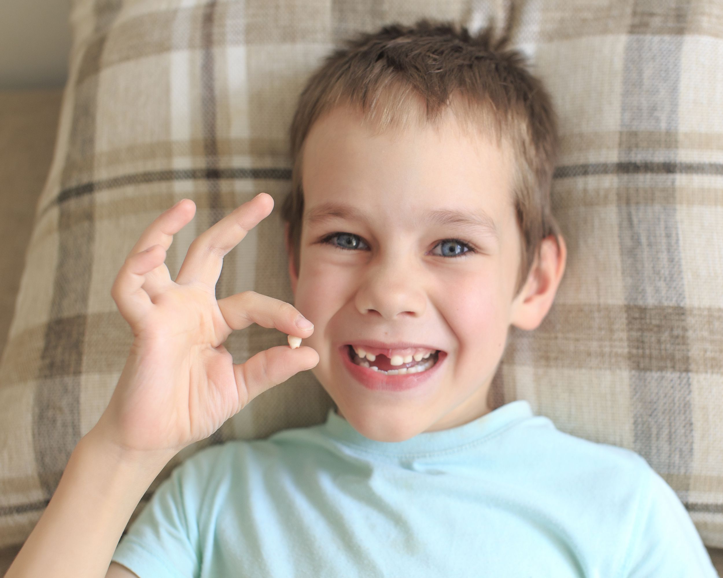 little boy in bed holding missing tooth and smiling