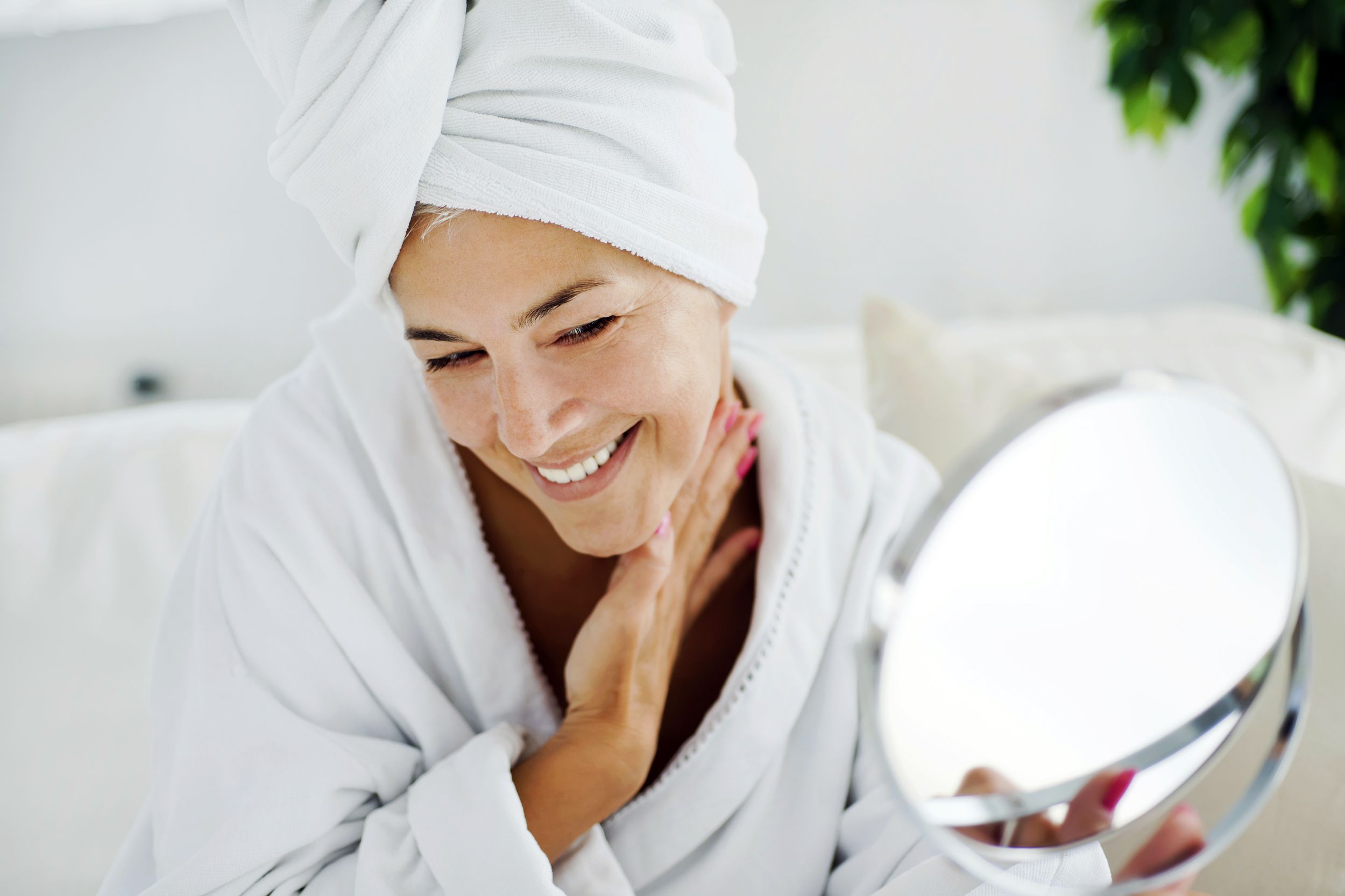 middle-aged woman smiling and wearing bathrobe while looking in the mirror